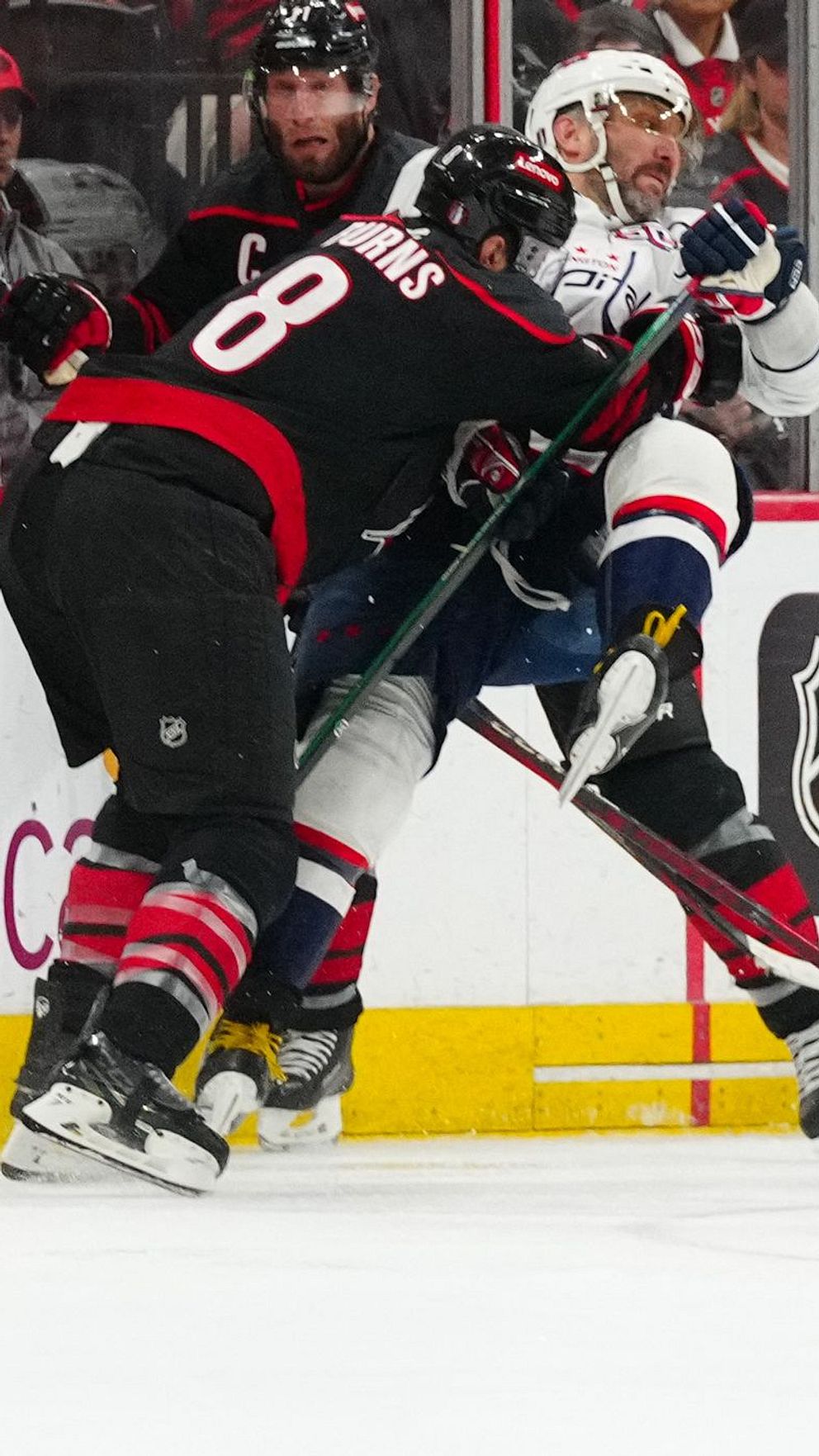 Ishockeyspelare kämpar om pucken vid sargen under en NHL-match med publik i bakgrunden.