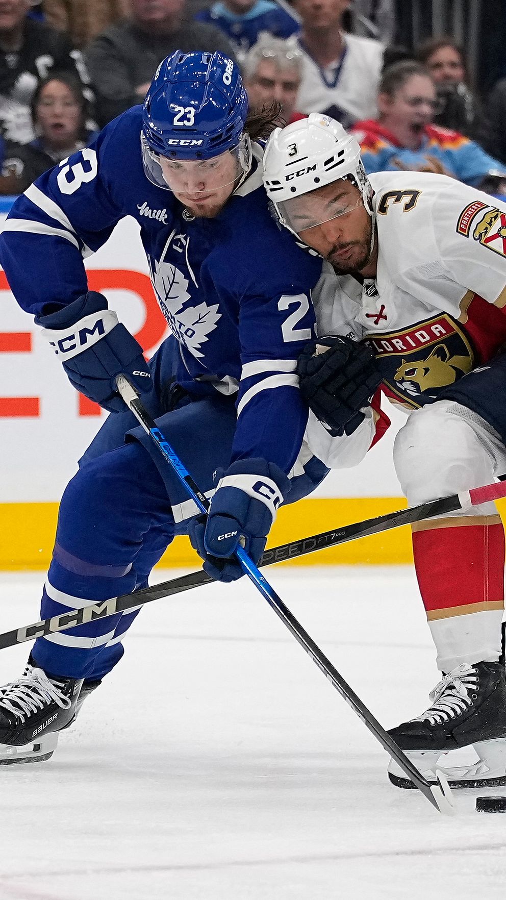 Två hockeyspelare från olika lag kämpar om pucken under en match.