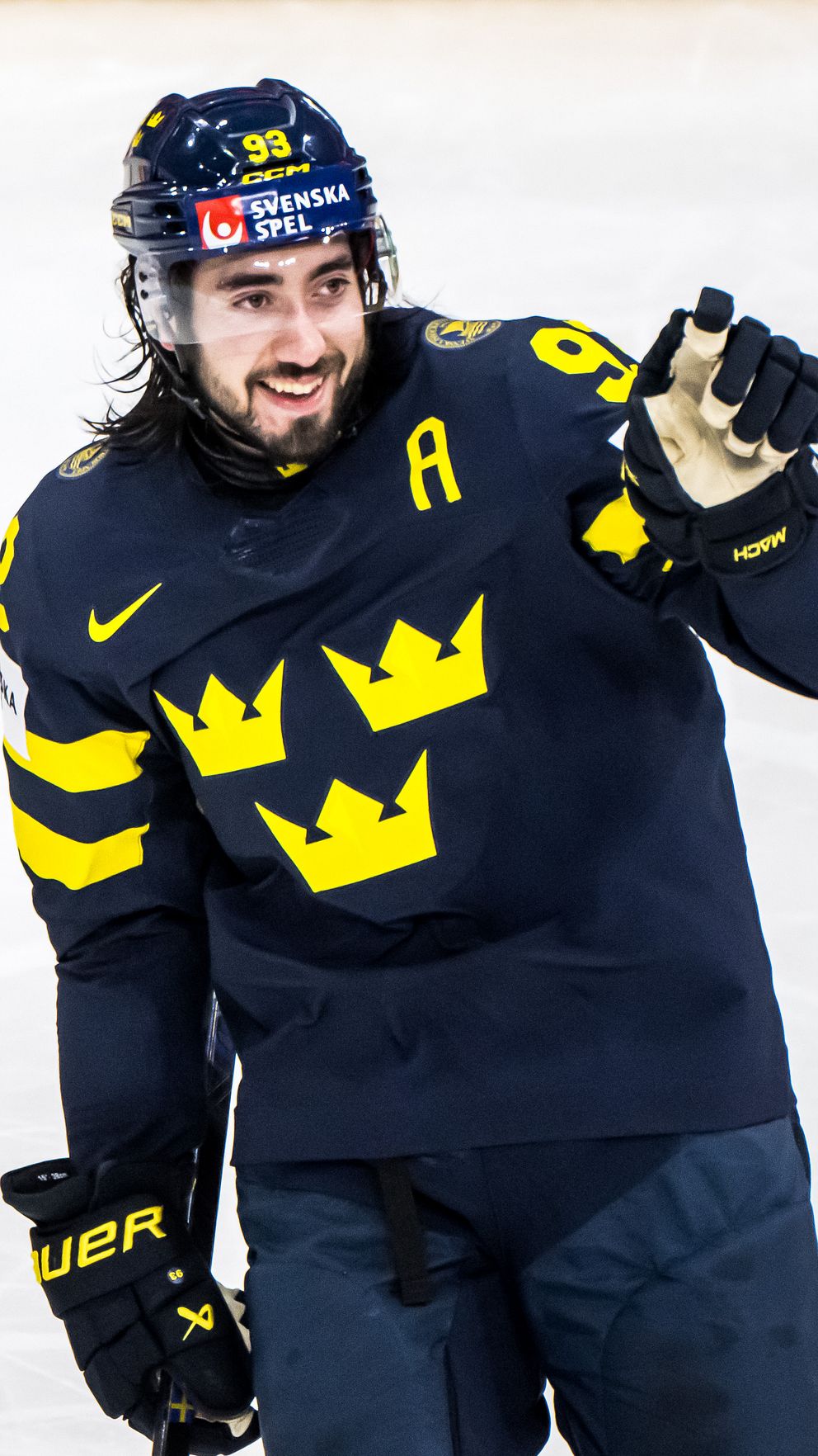 Svensk ishockeyspelare i Tre Kronor-tröja på isen, gör en gest med höger hand.