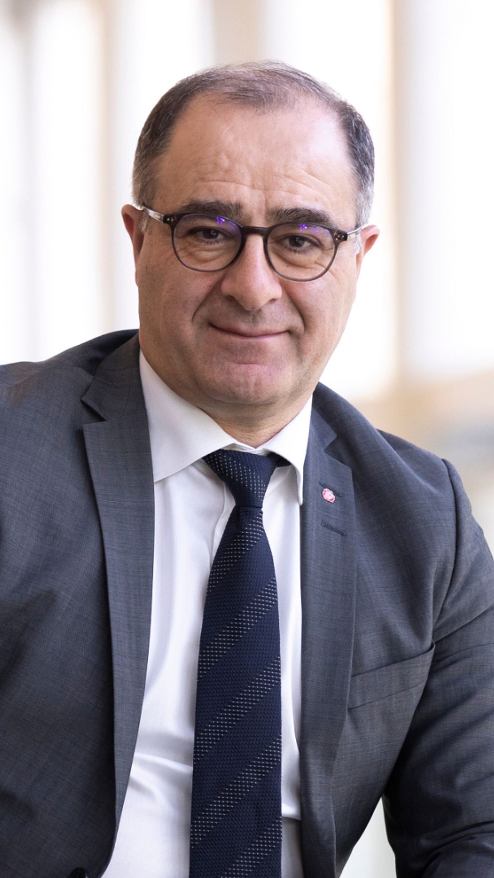Ilan de Basso (S) man med mörkt hår och glasögon iklädd kostym tittar in i kameran.