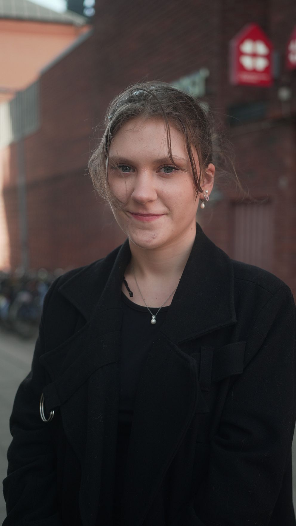 Ung kvinna i svart kappa framför ett tegelbyggnad med cyklar.