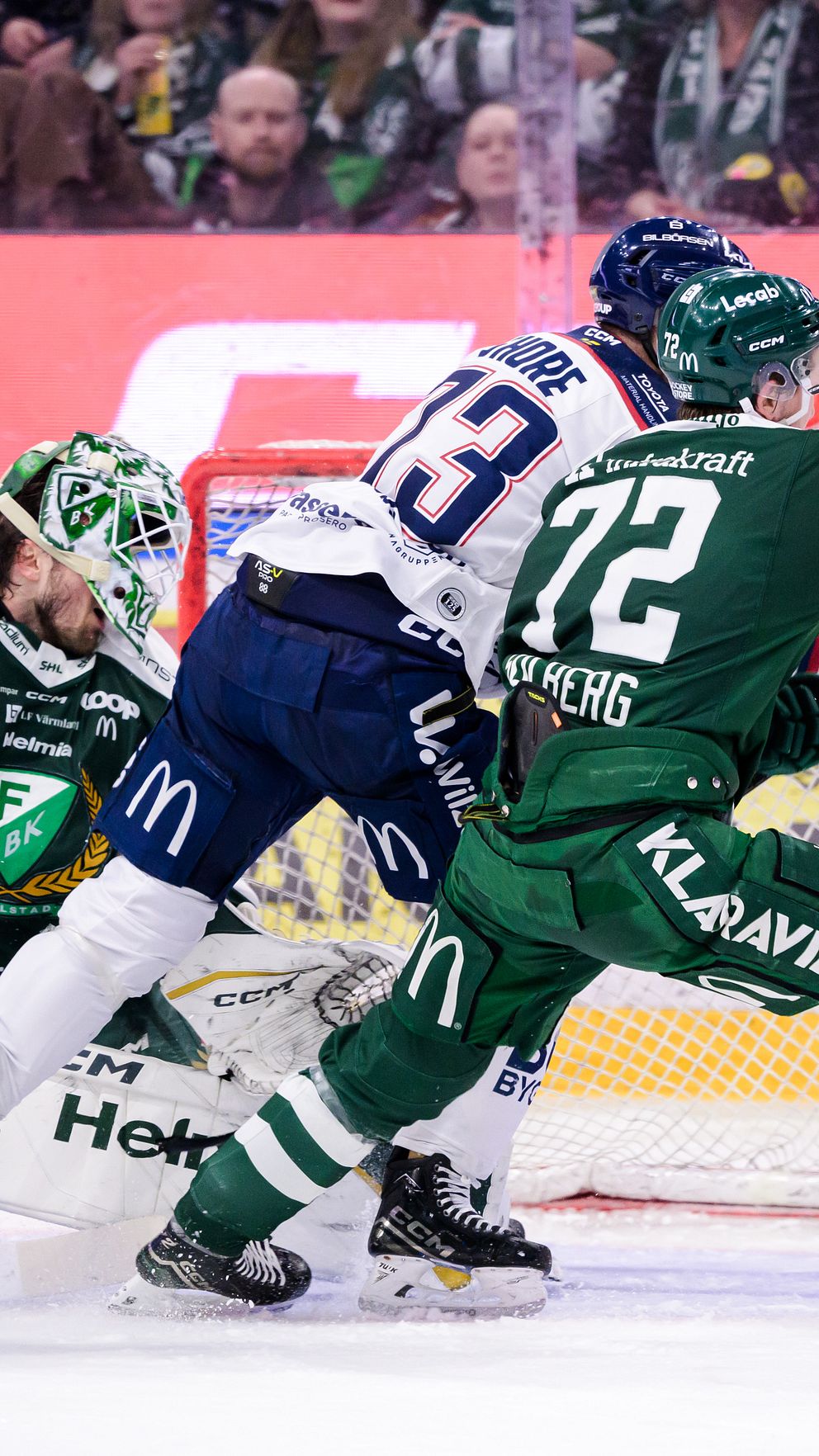Flera spelare i gröna matchställ försvarar sitt mål. En spelare i blått ställ åker rakt in i målet.