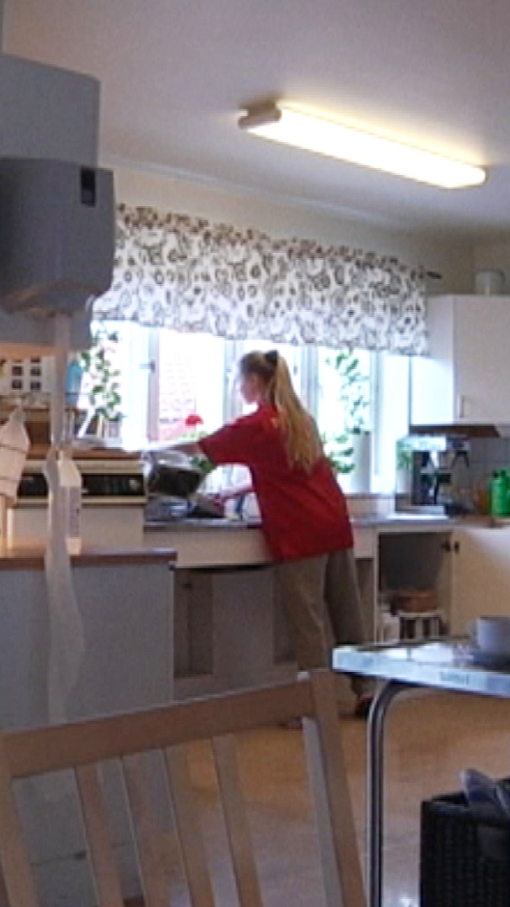Kvinna i röd tröja diskar i ett ljust och rymligt kök.