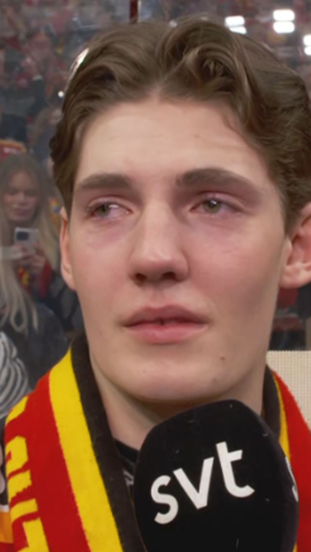 Hockeyspelare intervjuas av SVT efter match med jublande supportrar i bakgrunden.