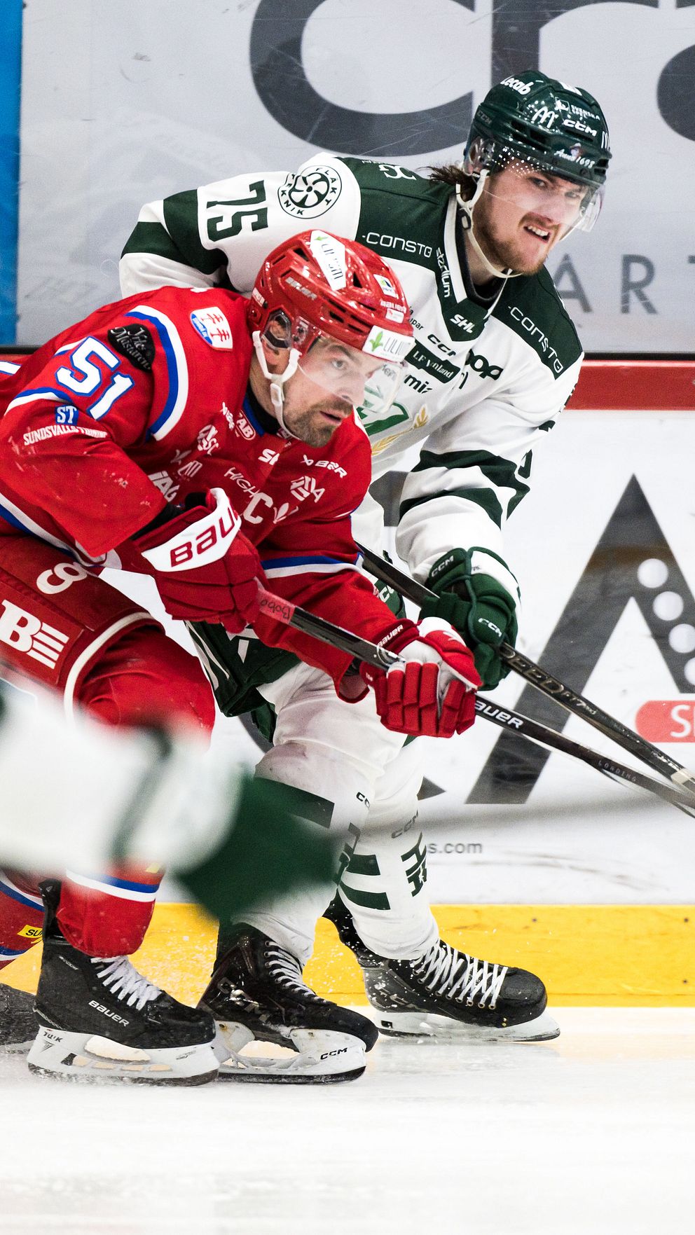 Två ishockeyspelare kämpar om pucken nära sargen under en match.