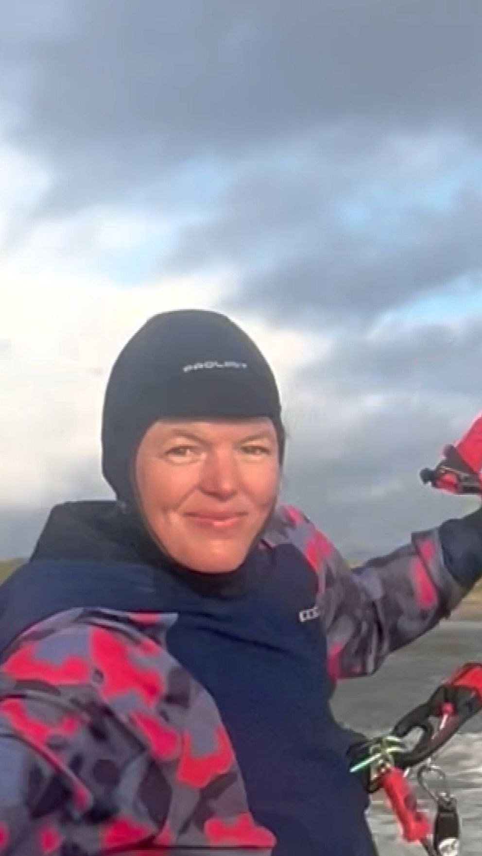 Person i färgglad jacka kitesurfar vid en stormig kust under molnig himmel.