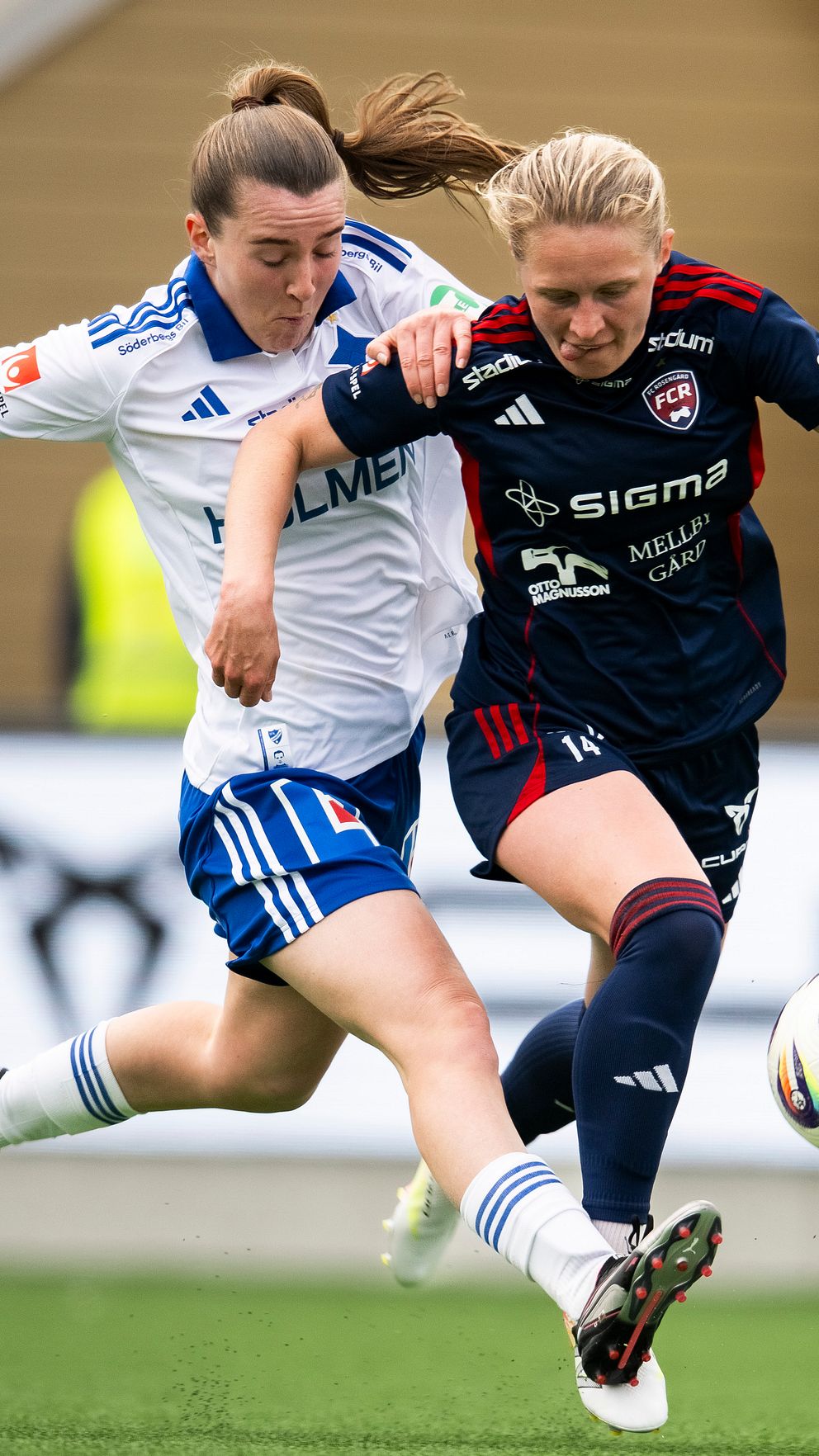 Två kvinnliga fotbollsspelare tävlar om bollen under en match på gräsplan.