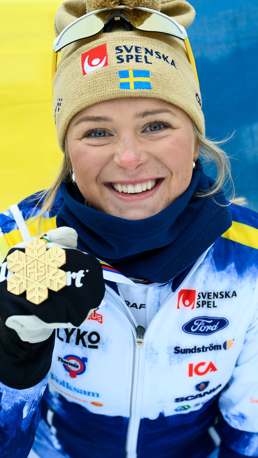 Idrottare visar medalj framför svensk flagga.