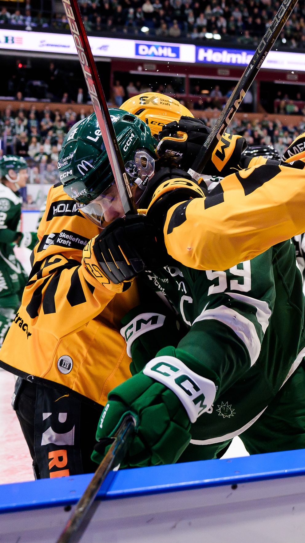 Ishockeyspelare i närkamp intill sargen under pågående match. Stämningen är intensiv och tuff.