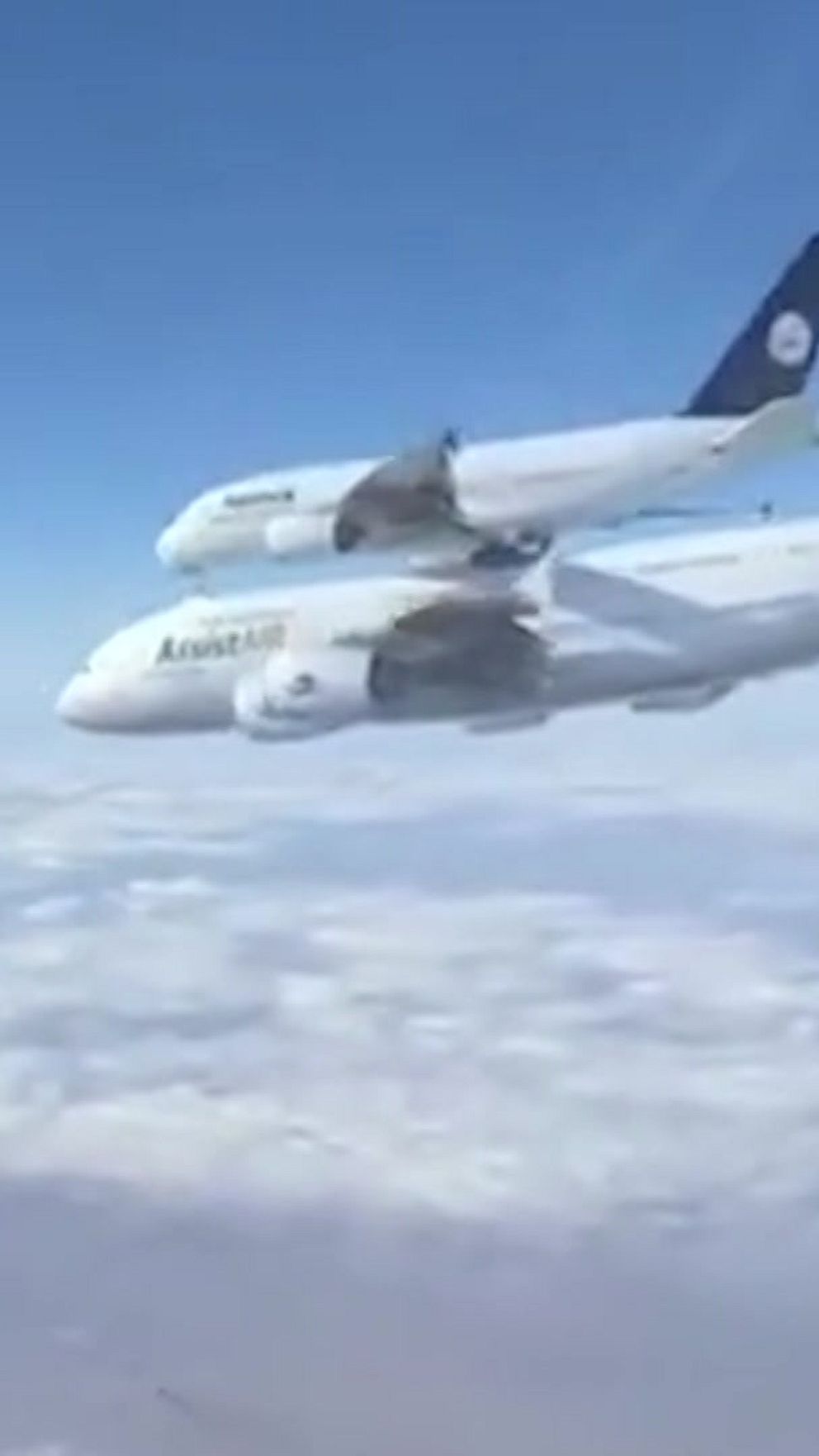 Ett flygplan av modellen Airbus A380 är på väg upp i luften, med ett annat mindre flygplan ovanpå det stora planet. Bakgrunden visar en klar blå himmel och ett vitt molntäcke som sträcker sig över marken.