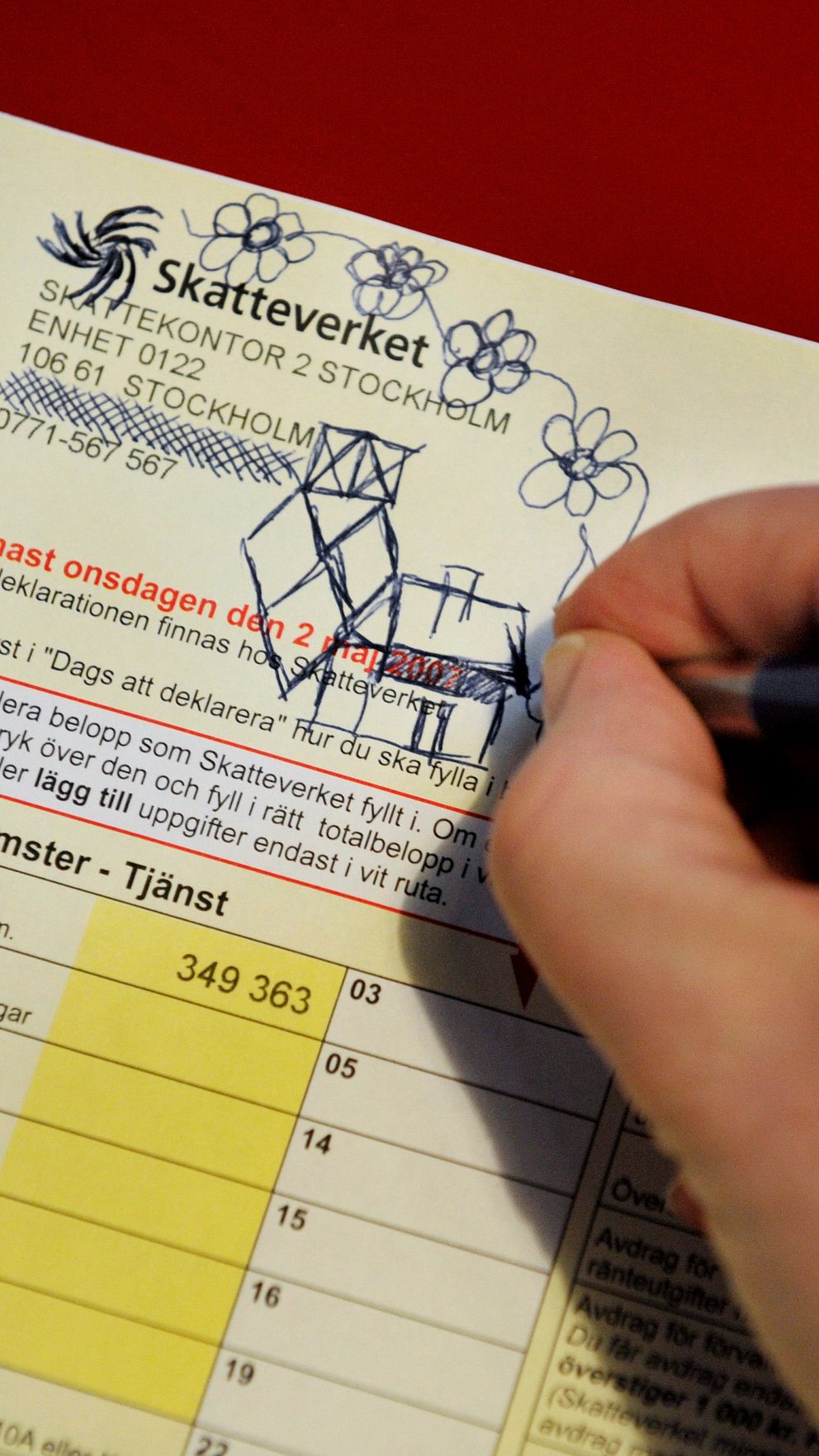 En hand håller i en penna och ritar figurer och blommor på en inkomstdeklaration från Skatteverket.