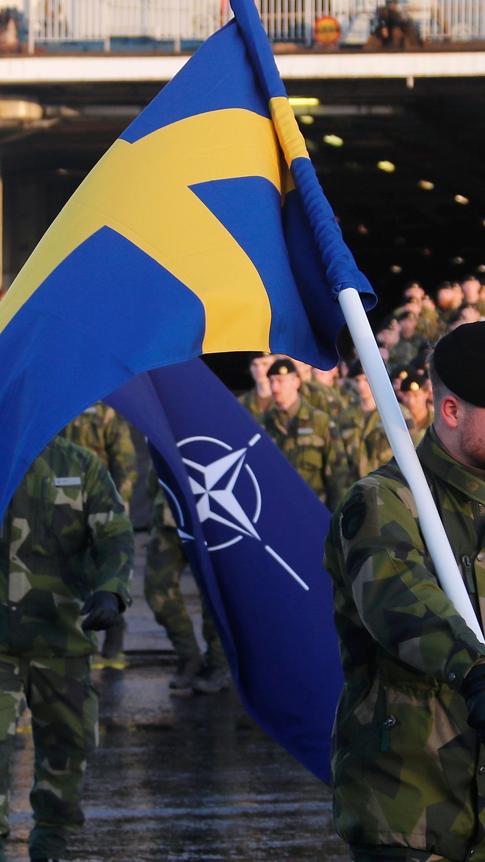 Svenska soldater med flaggor från Sverige och NATO går av fartyg.