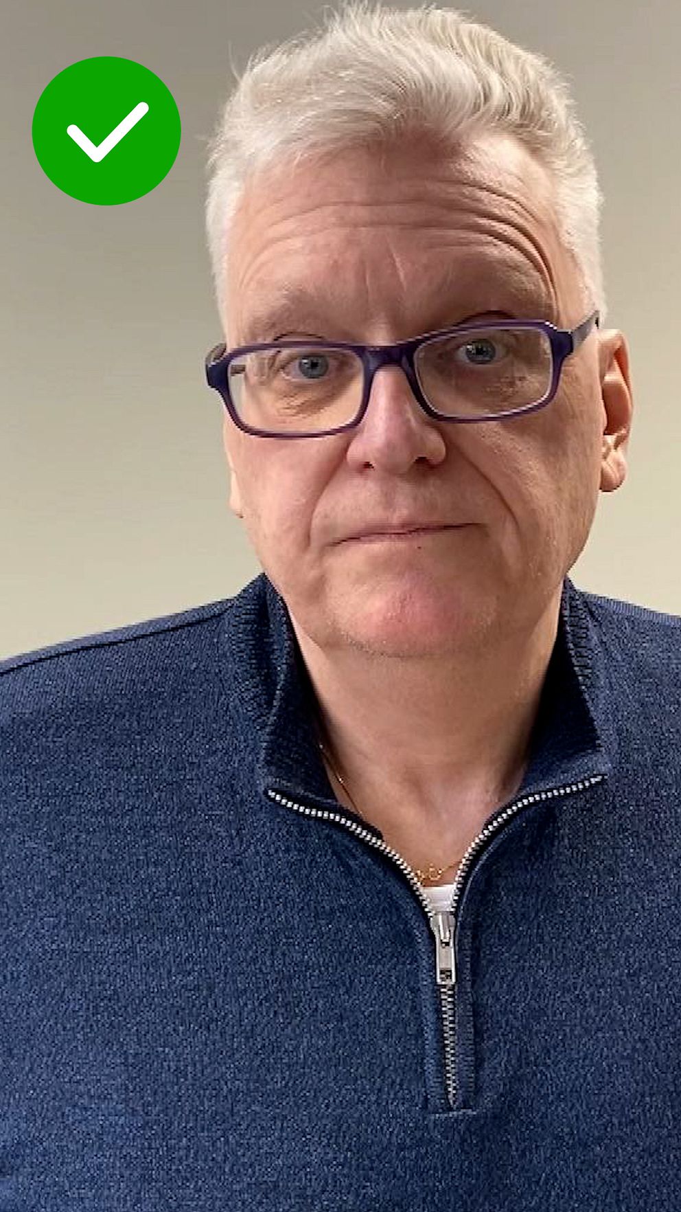 Person i blå dragkedjetröja med grått hår, grå bakgrund och en grön checkmark i hörnet.