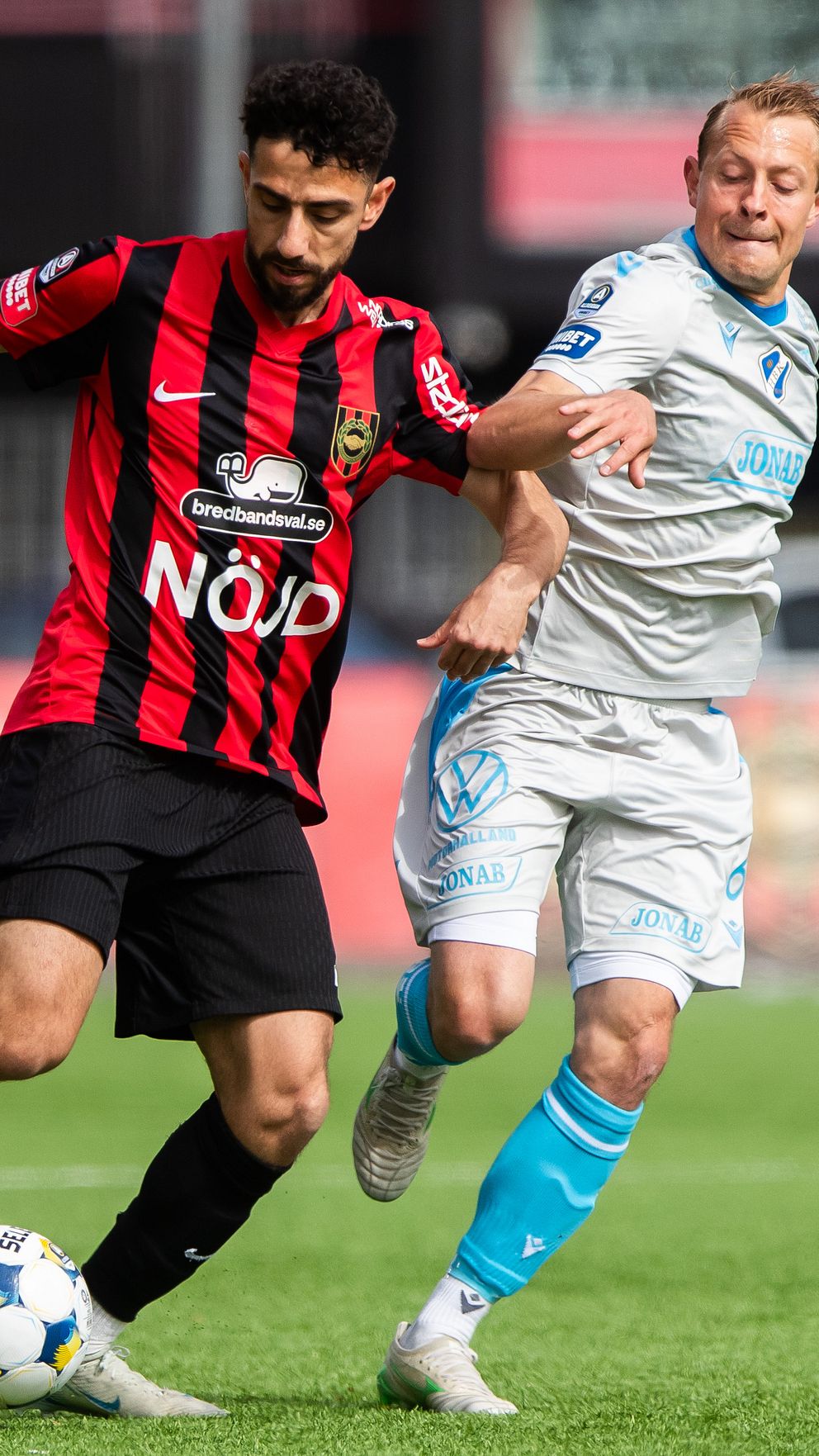 Två fotbollsspelare i kamp om bollen under en match på gräsplan.