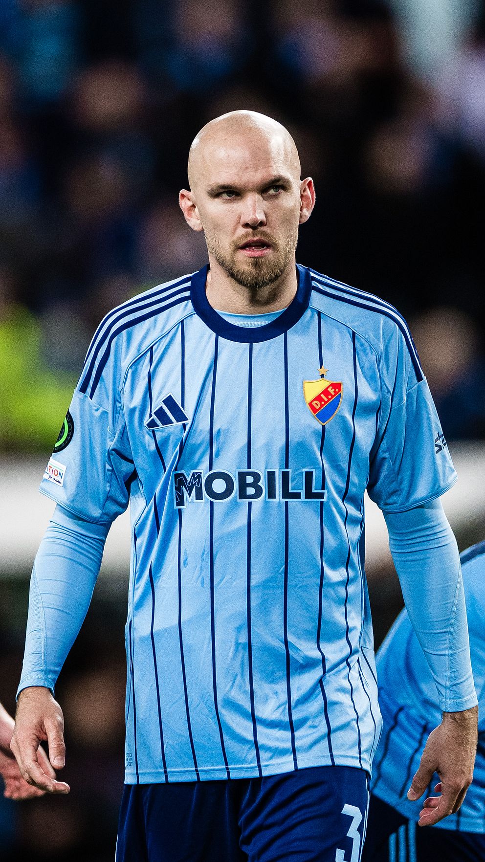 Tre Djurgården-spelare diskuterar på fotbollsplan under en match i blå matchställ.