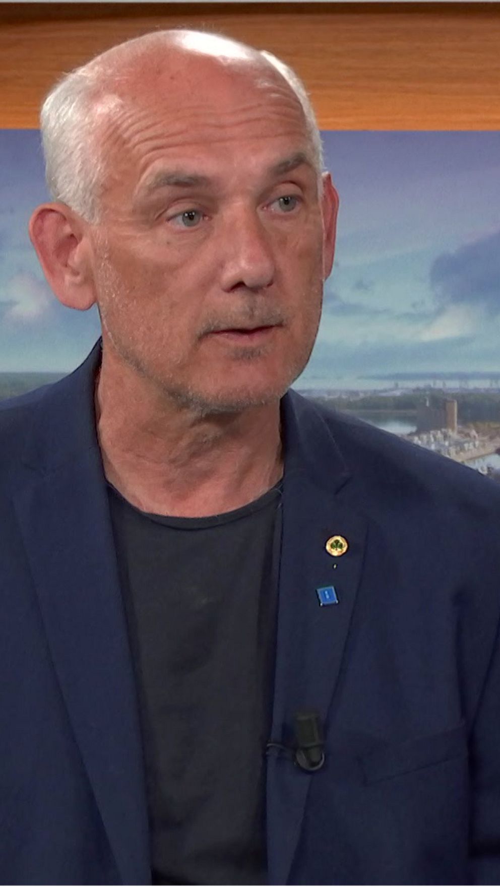 Man, Mikael Bäckström, står i en studio. Grått hår och iklädd kavaj.