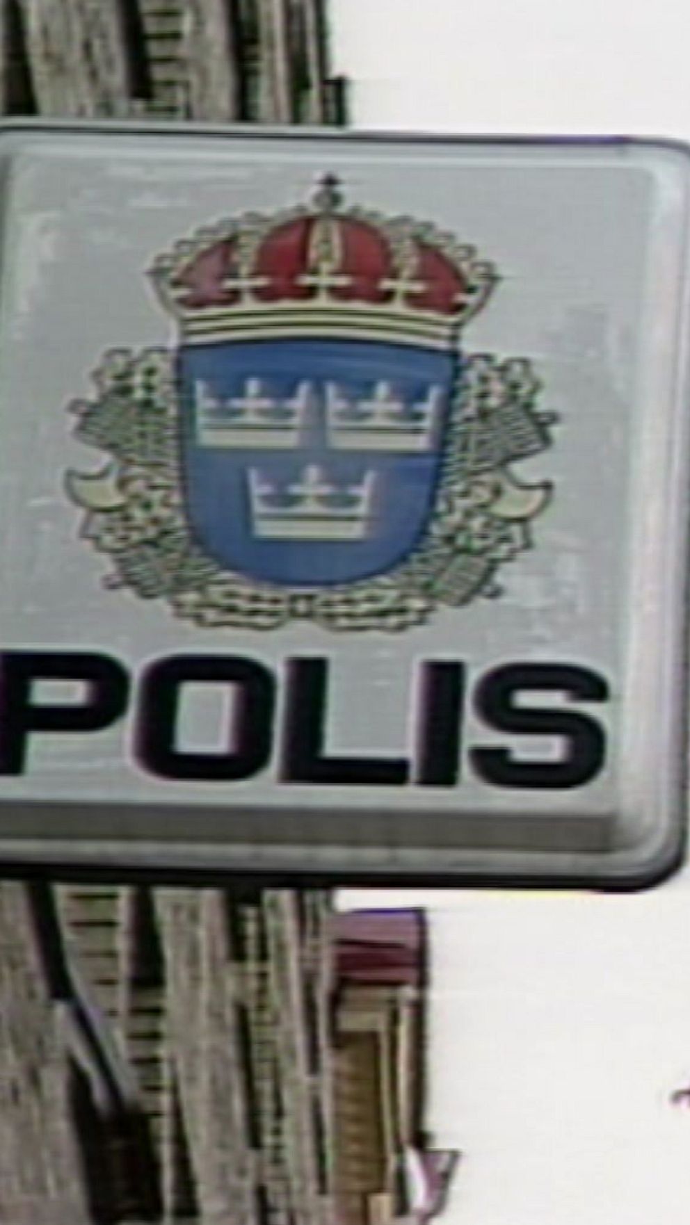 Gammal skylt med polisens emblem på byggnadsvägg.