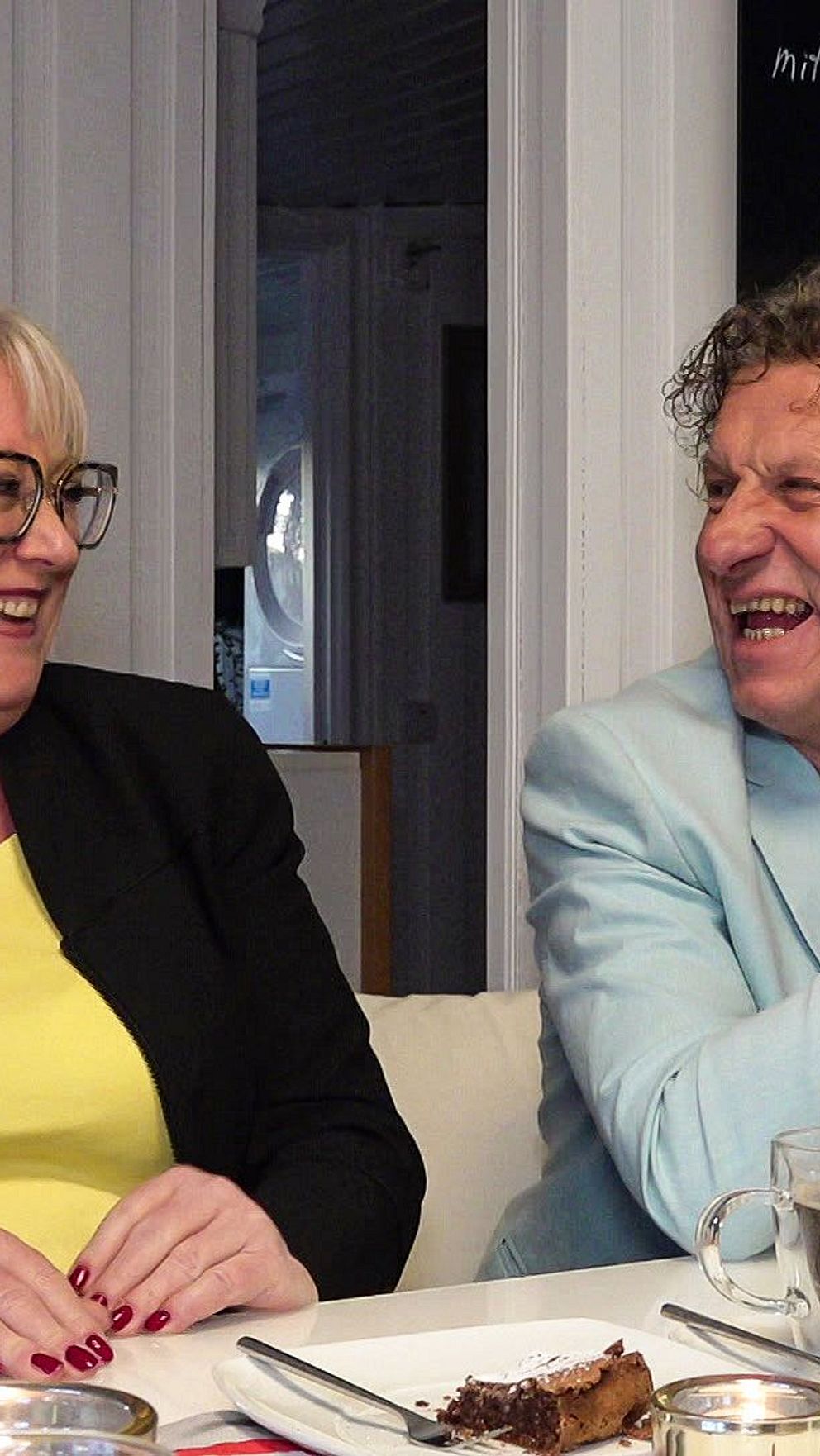 Edith och Udo Hitzke sitter vid sitt köksbord och kollar på varandra och skrattar