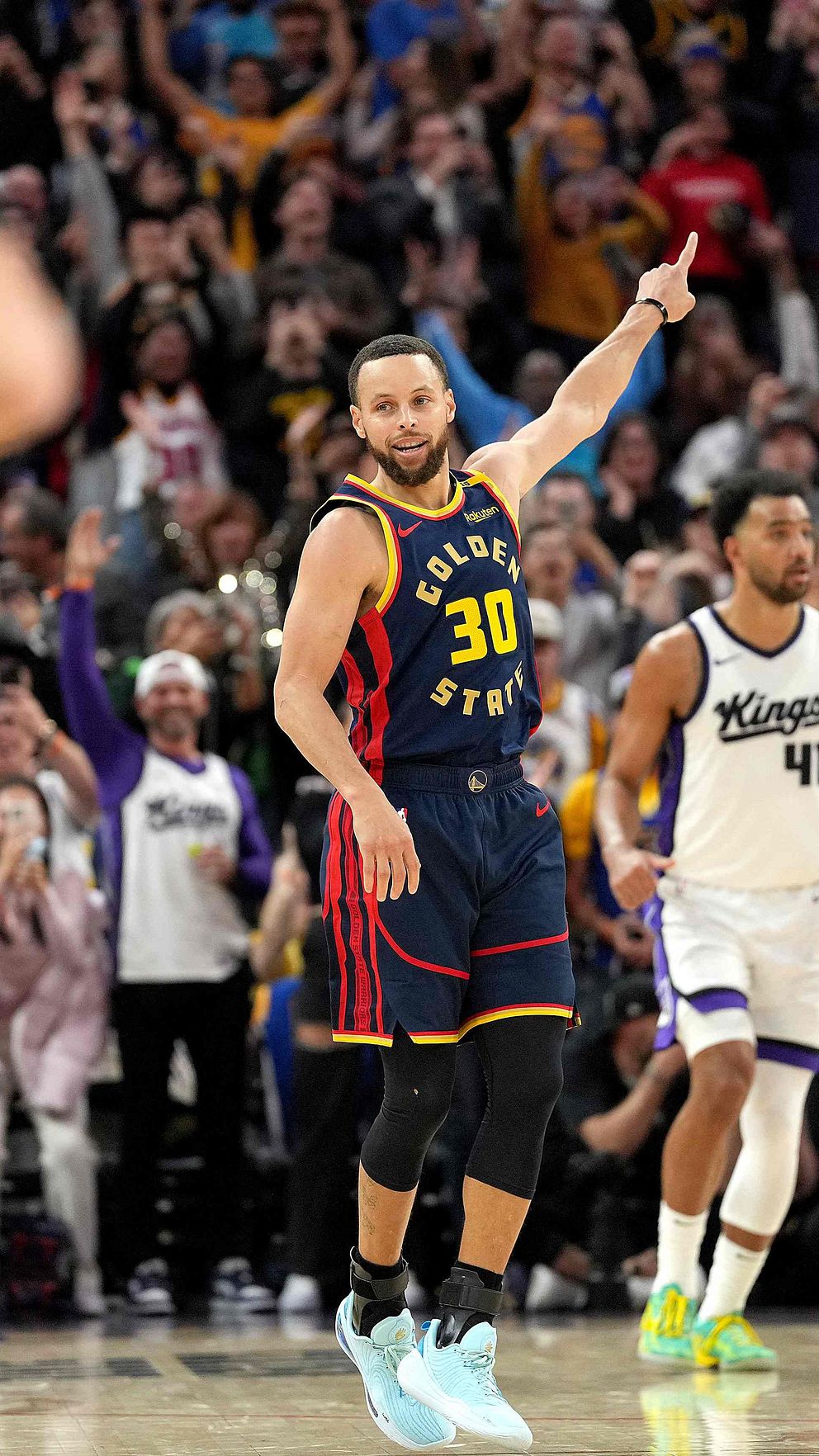 Basketbollspelare firar efter att ha gjort poäng under en match med publikjubel i bakgrunden.