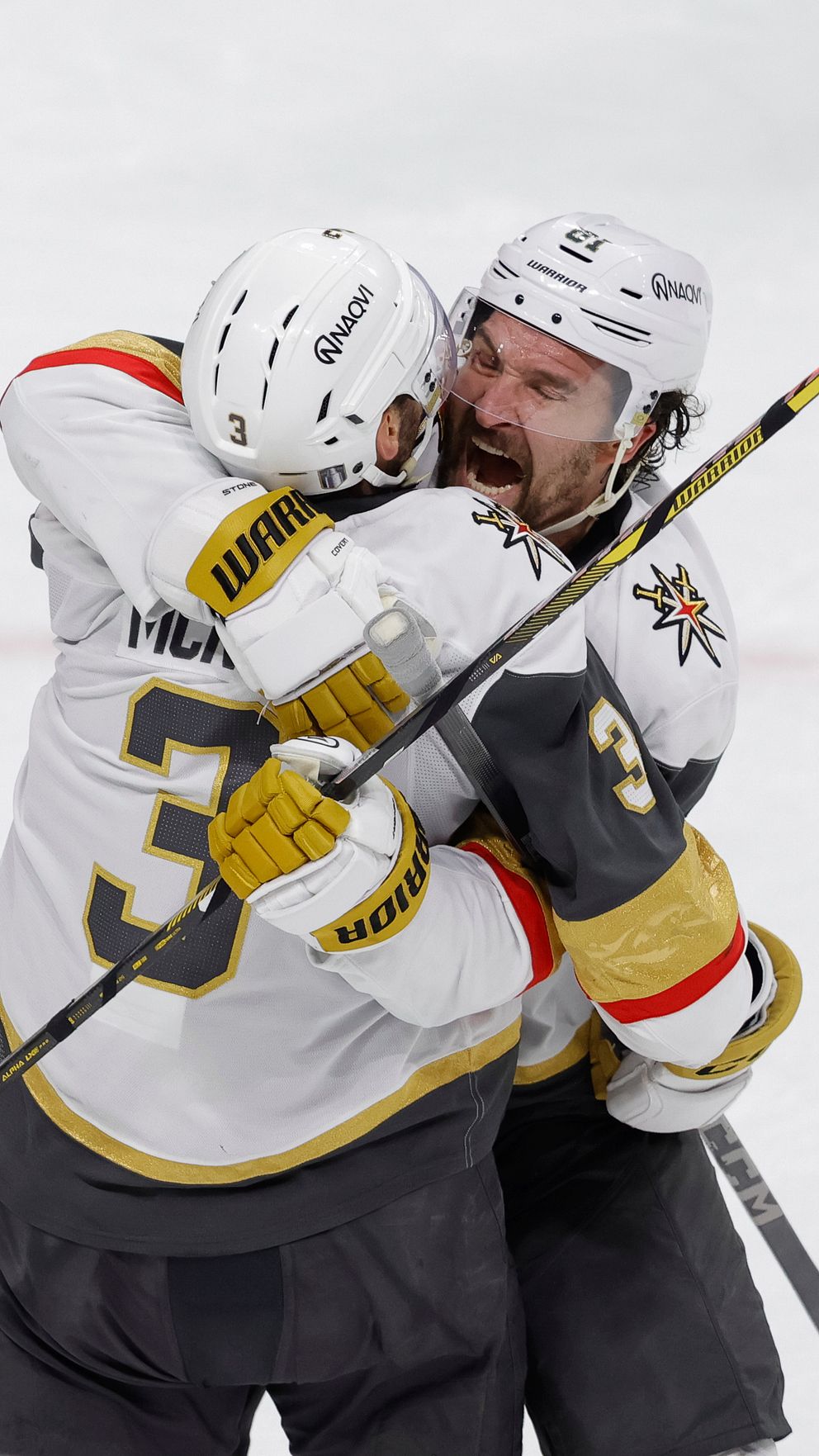 Två ishockeyspelare i vitt omfamnar varandra på isen efter mål.