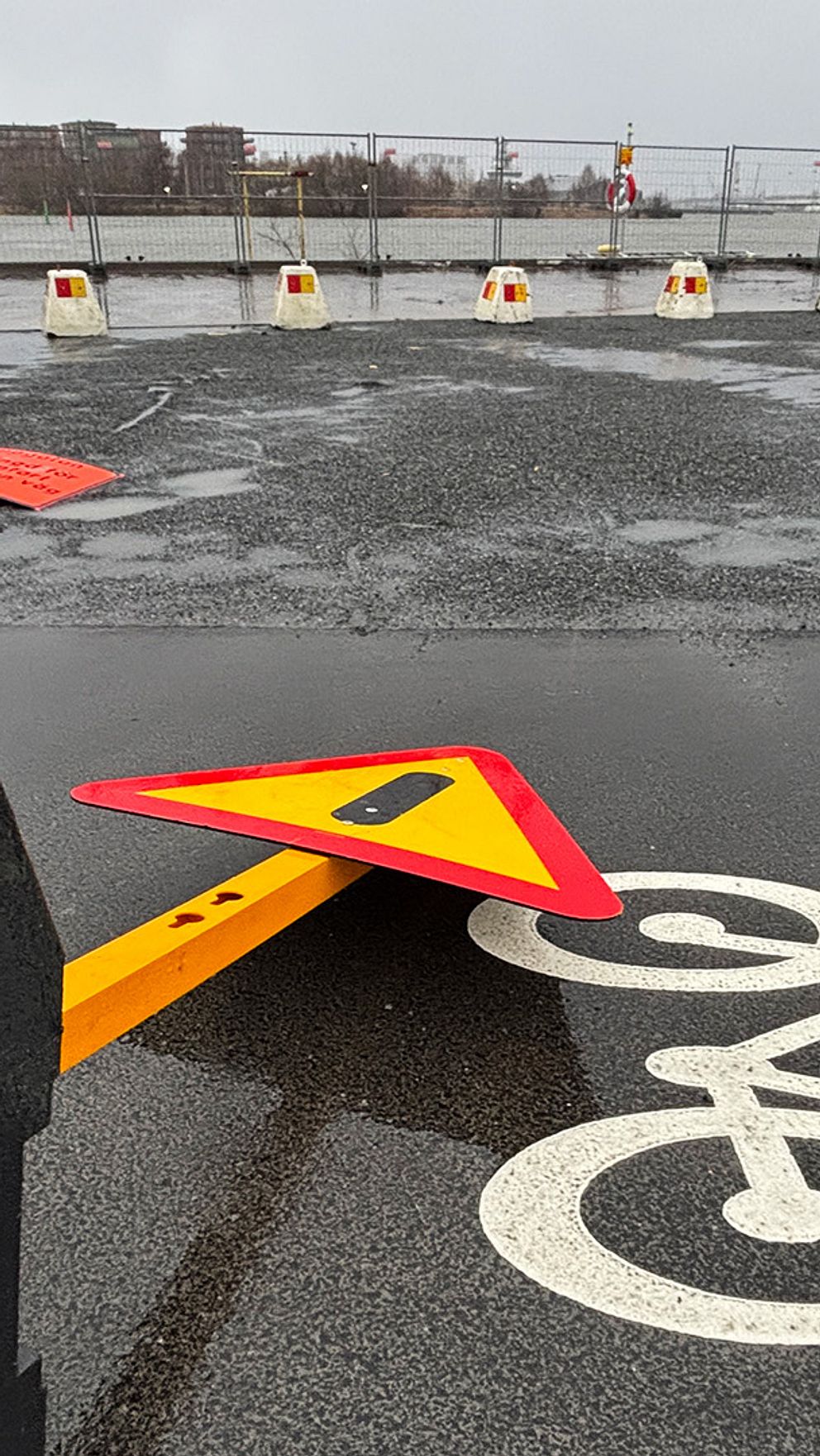 En vägskylt som har vält på en cykelbana i Göteborg, med regnvattensamling på asfalt. I bakgrunden syns cykelbanemärke och avspärrningar.