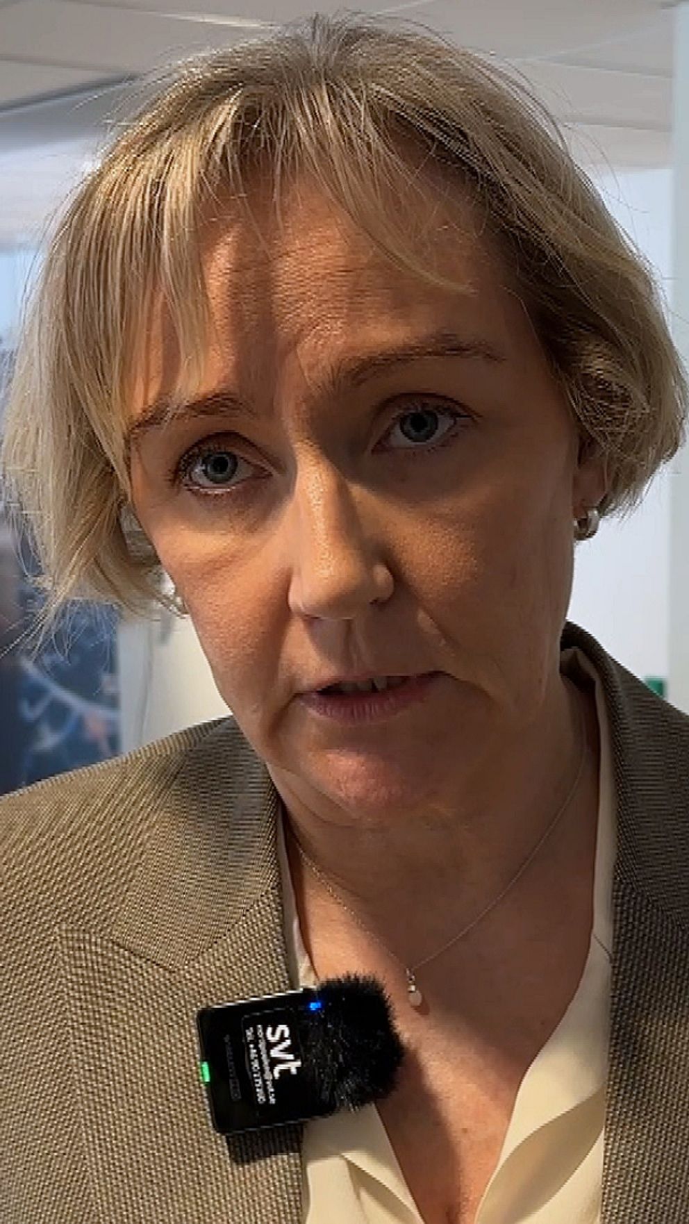 Landshövdningen Helene Hellmark Knutsson står i ett fullt konferensrum, i bakgrunden står journalister och pratar med kommunpolitiker och tjänstepersoner.