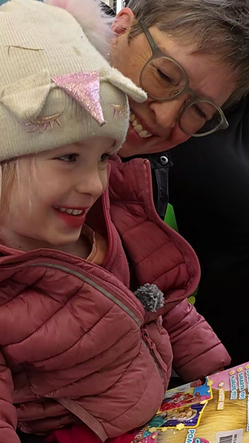 Lova Westerlund, fem år,  i rosa jacka med tidskrift sitter i farmor Annelie Westerlunds knä i bokbussen.