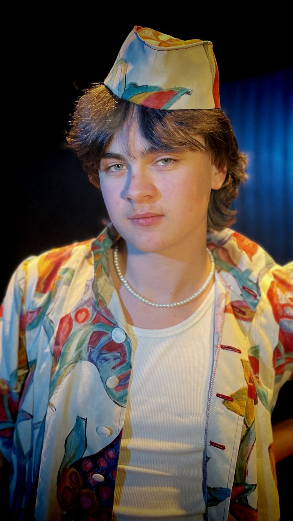 Person, Dennis Skoglund, i färgstark utstyrsel och hatt på scen under stark belysning.