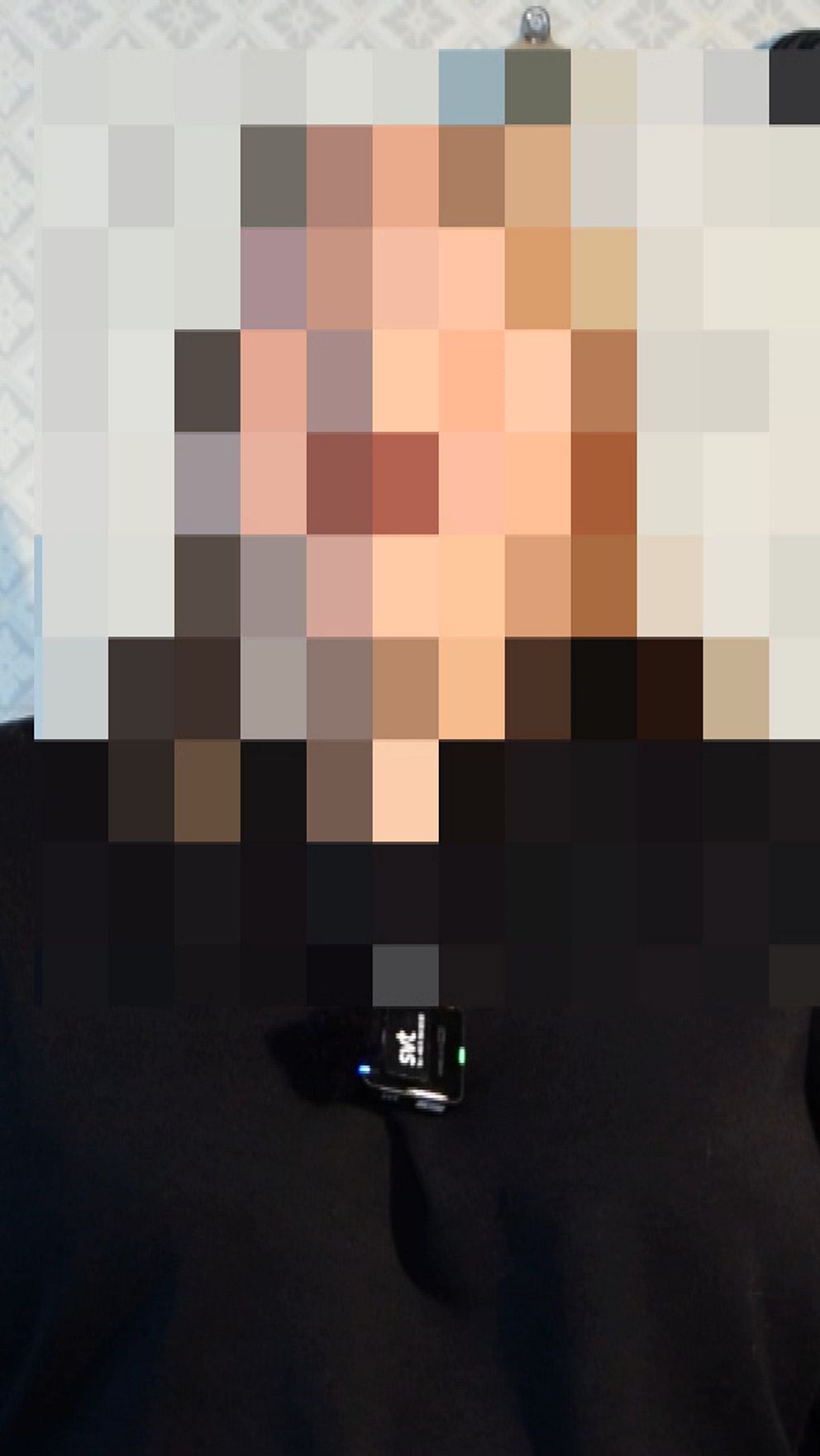 En person med pixlat ansikte framför en dörr och vitmönstrad tapet.