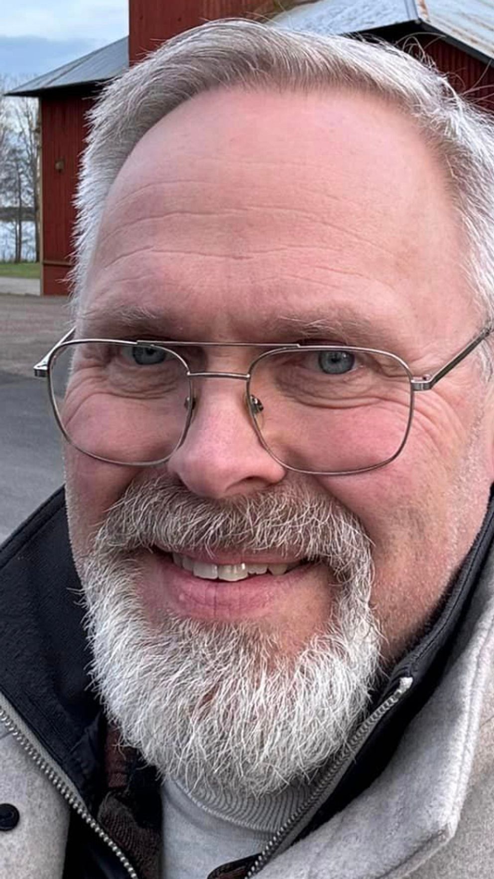 Man, Raymond Pettersson, grått hår ock skägg. Tittar in i kameran och ler.