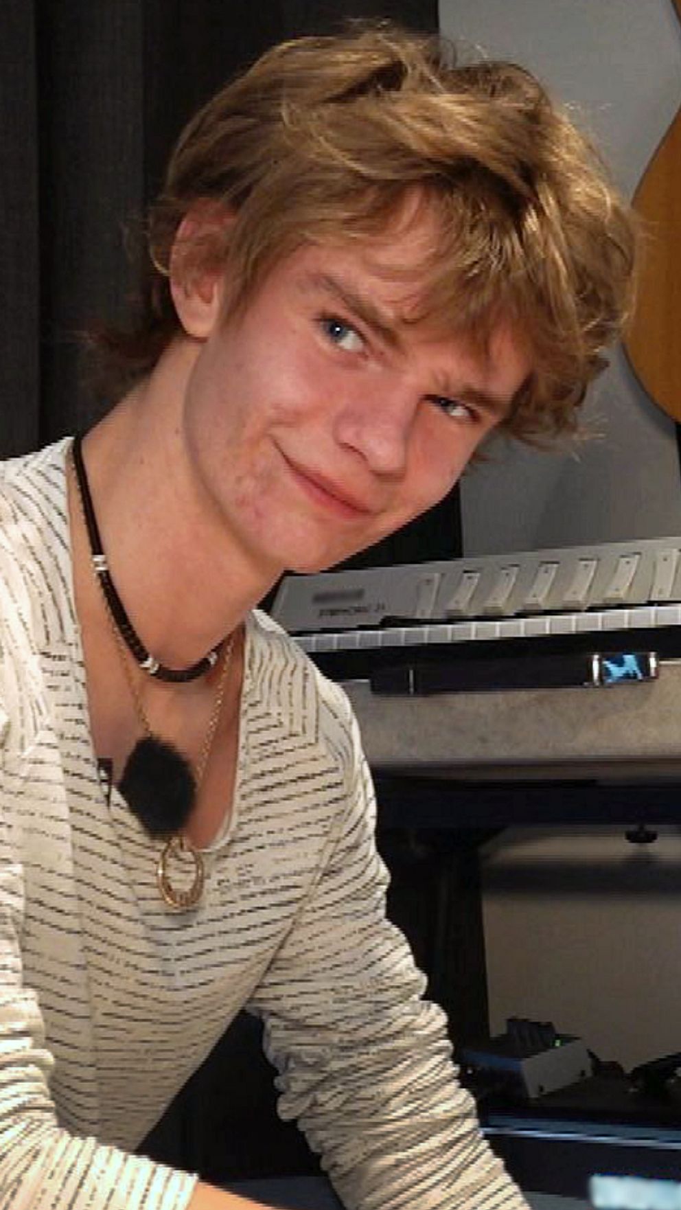 Person sitter bredvid musikutrustning i ett rum med gitarr på väggen.