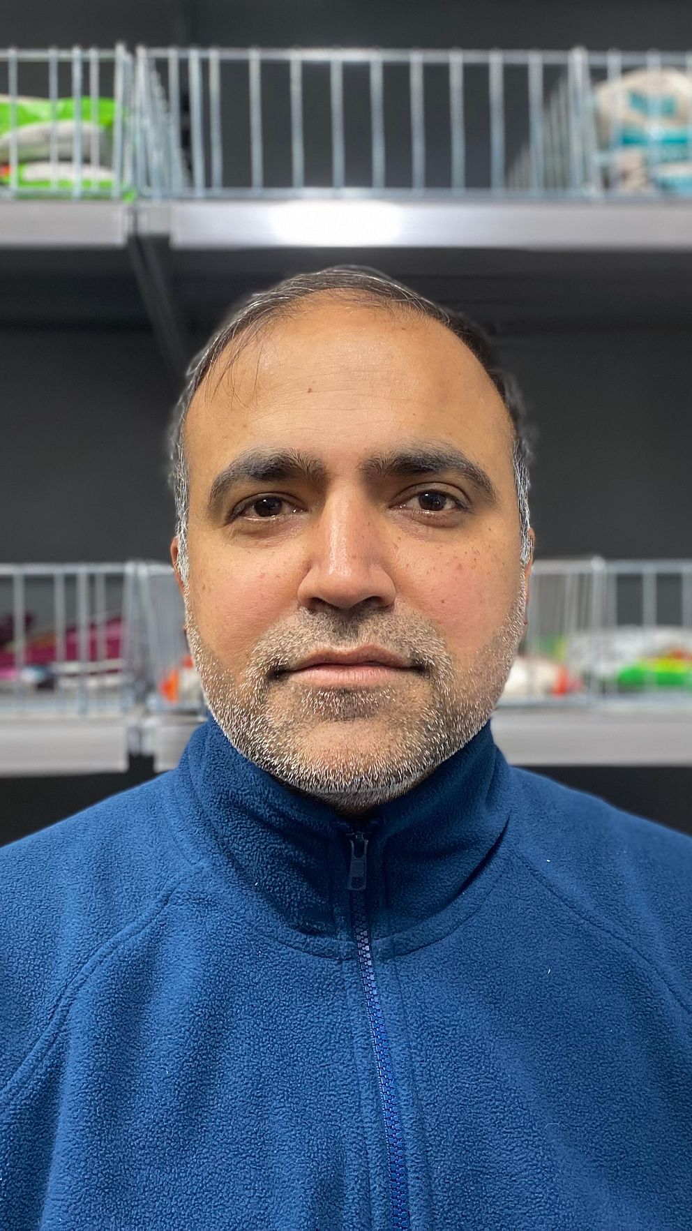 Chetan Sharma i sin indiska matbutik i Skellefteå. Han bär en blå fleecetröja och i bakgrunden syns butikshyllor med mat.