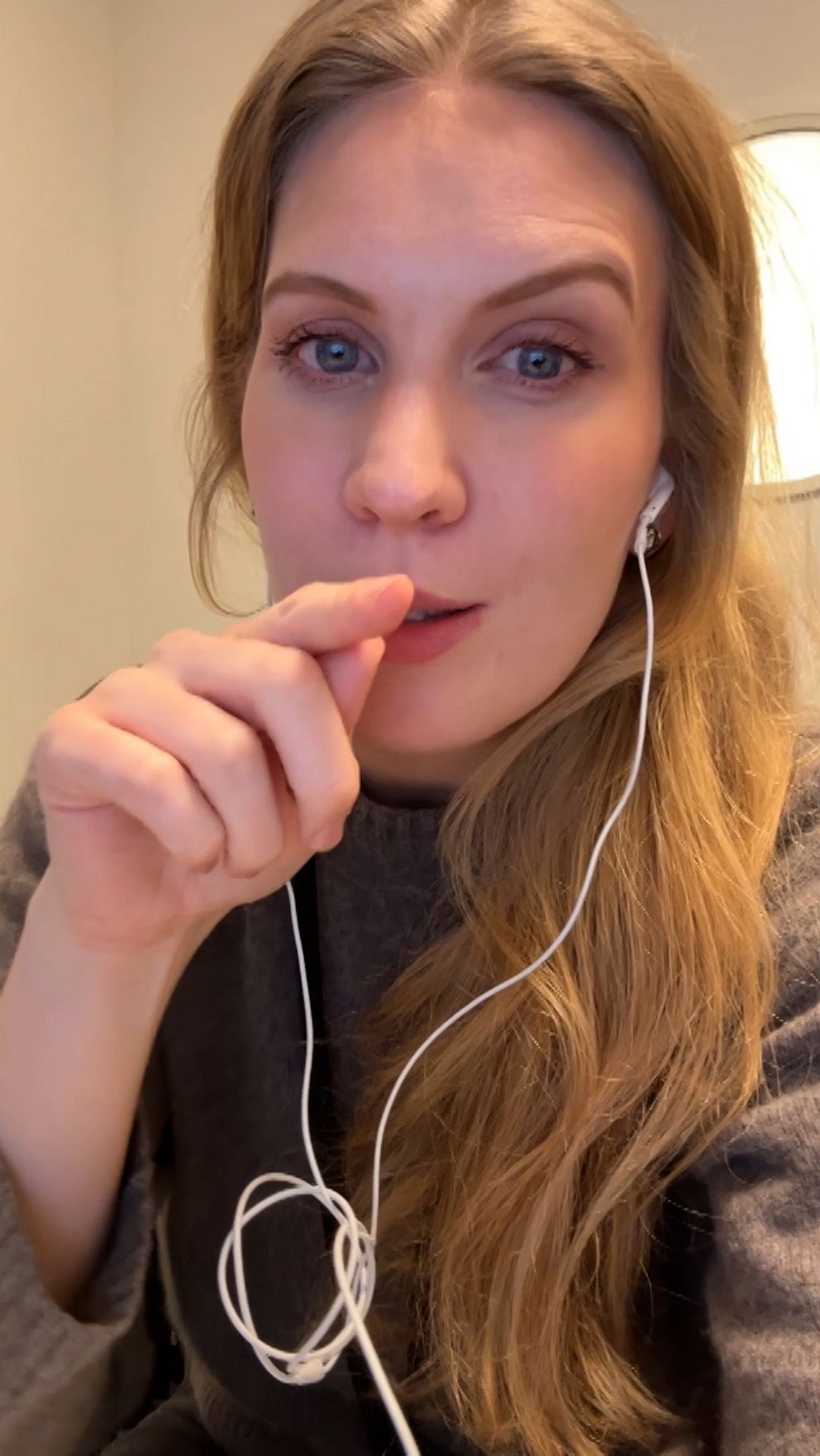 Person med lång blont hår håller i en laddningskabel med ett gråt tyg plagg.
