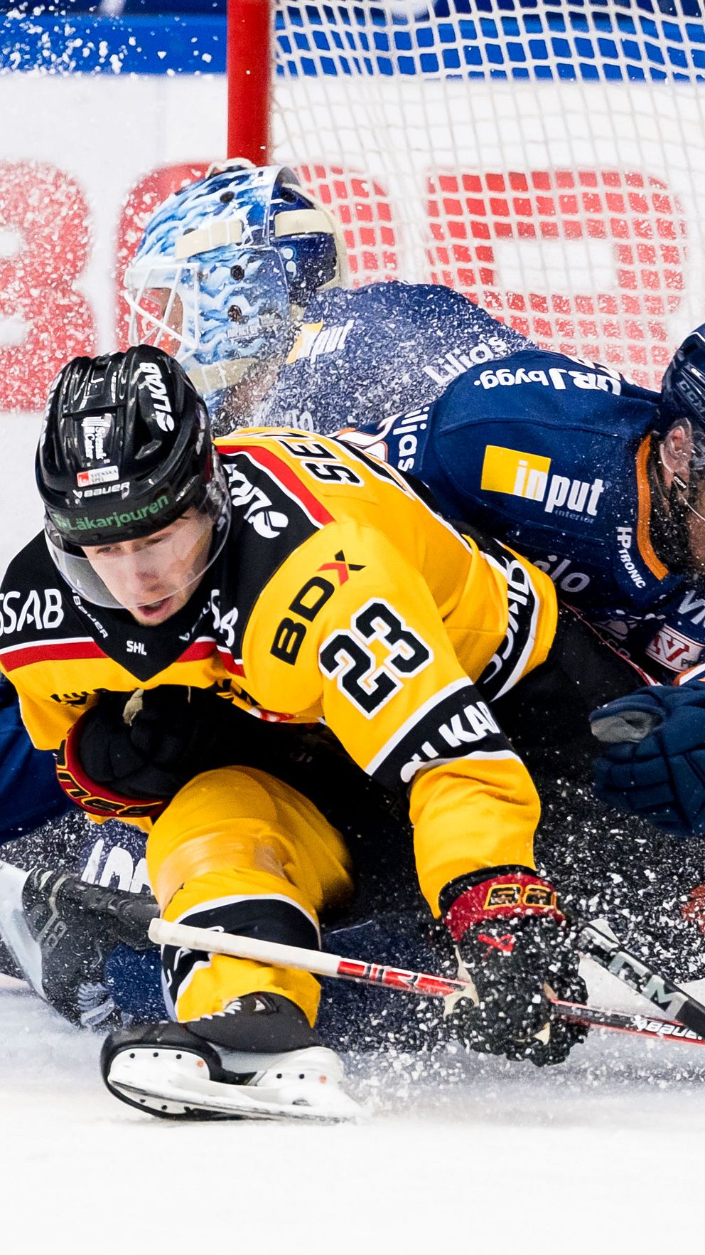 Islandojkrävning mellan två hockeyspelare vid målet. Målvakt observerar spelet.