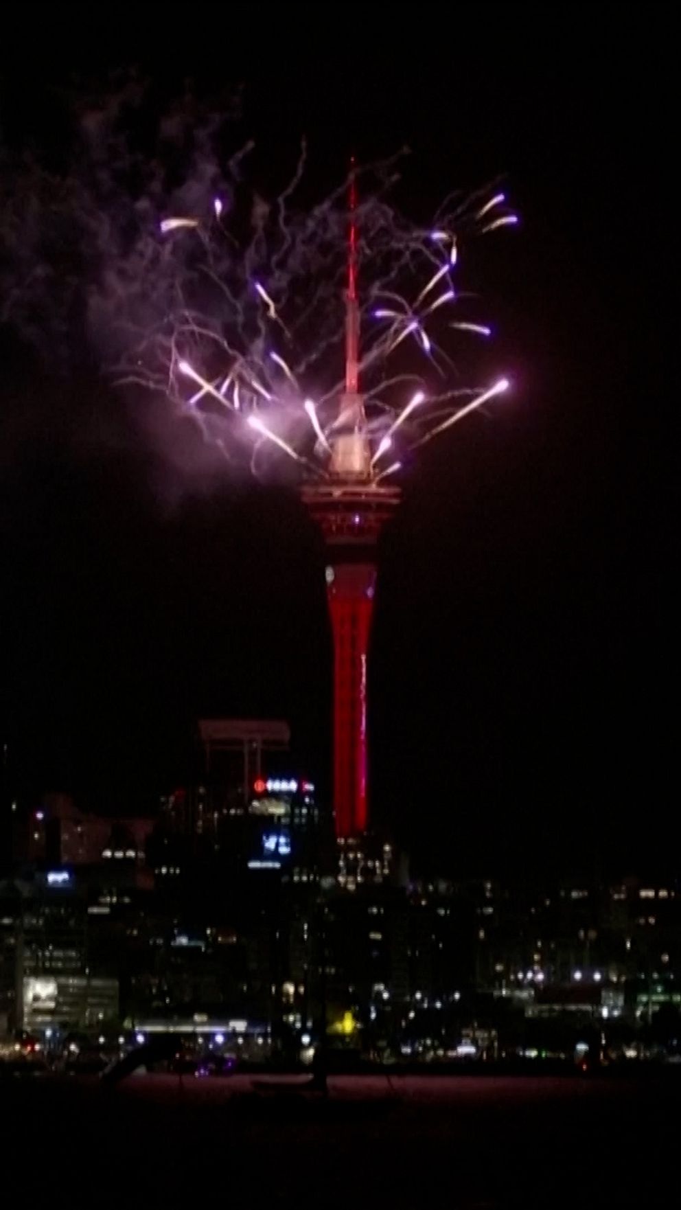 Fyrverkerier sprakar över Sky Tower i Auckland under natten, med stadens ljus som bakgrund.