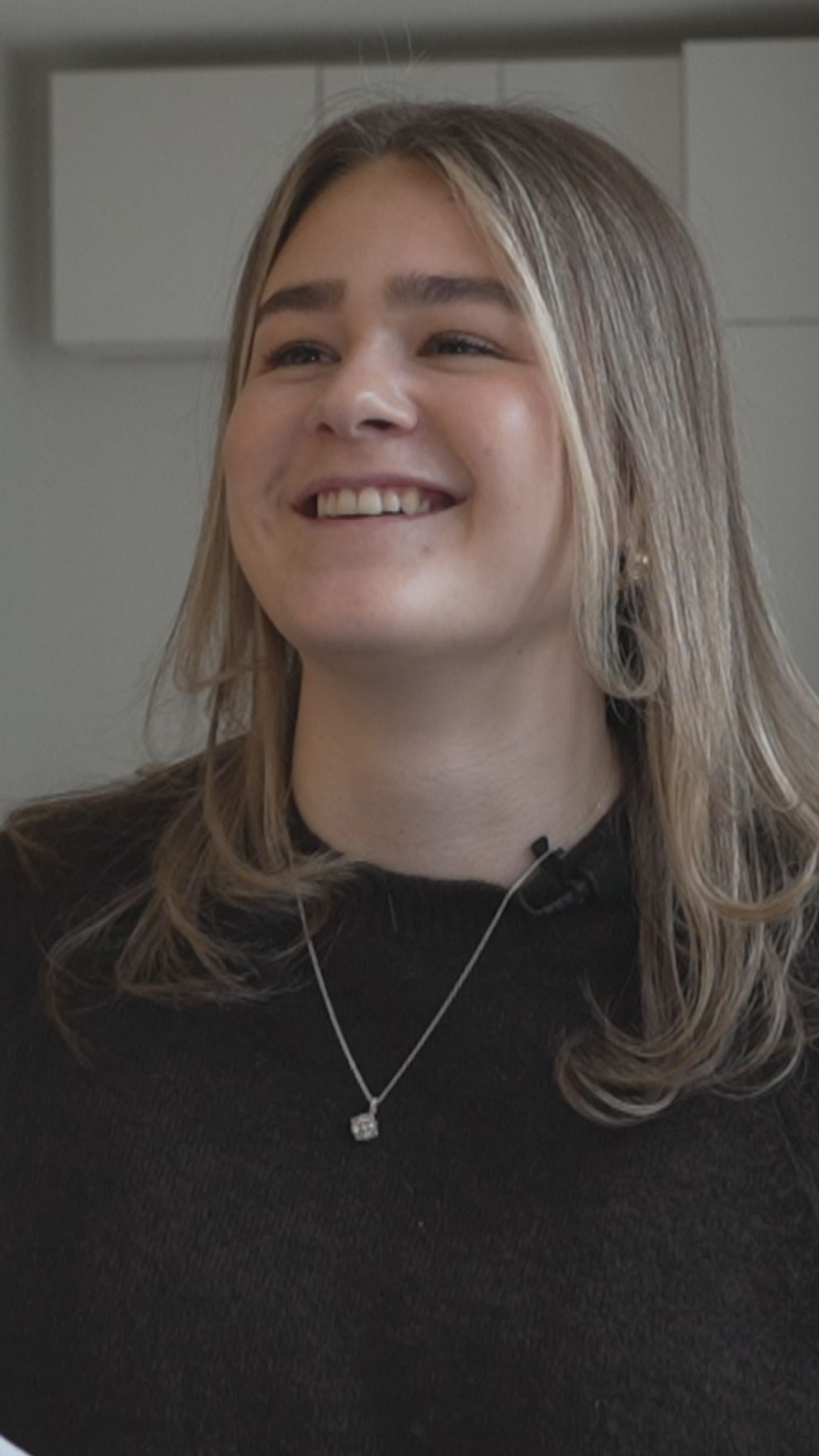 Person i mörk tröja sitter i välbelyst rum med mjukt inredda möbler.
