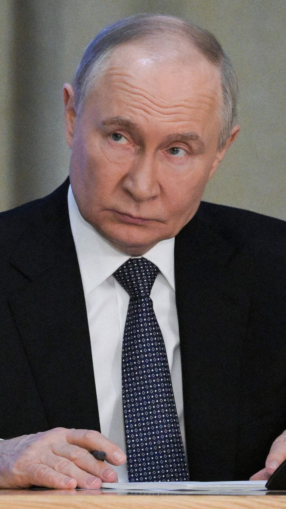 Vladimir Putin i kostym vid mikrofon i en formell miljö.