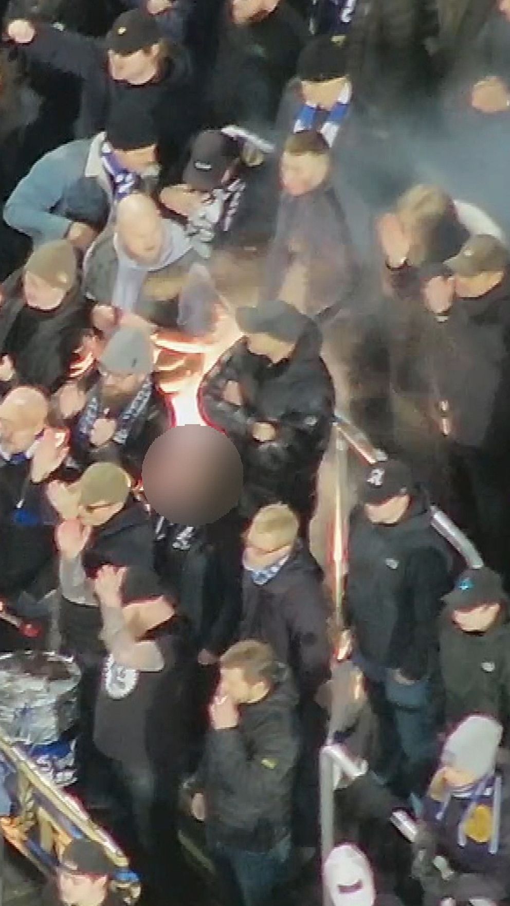 Folksamling klädd i mörka kläder, med någon hållande en fackla, omgiven av rökmoln.