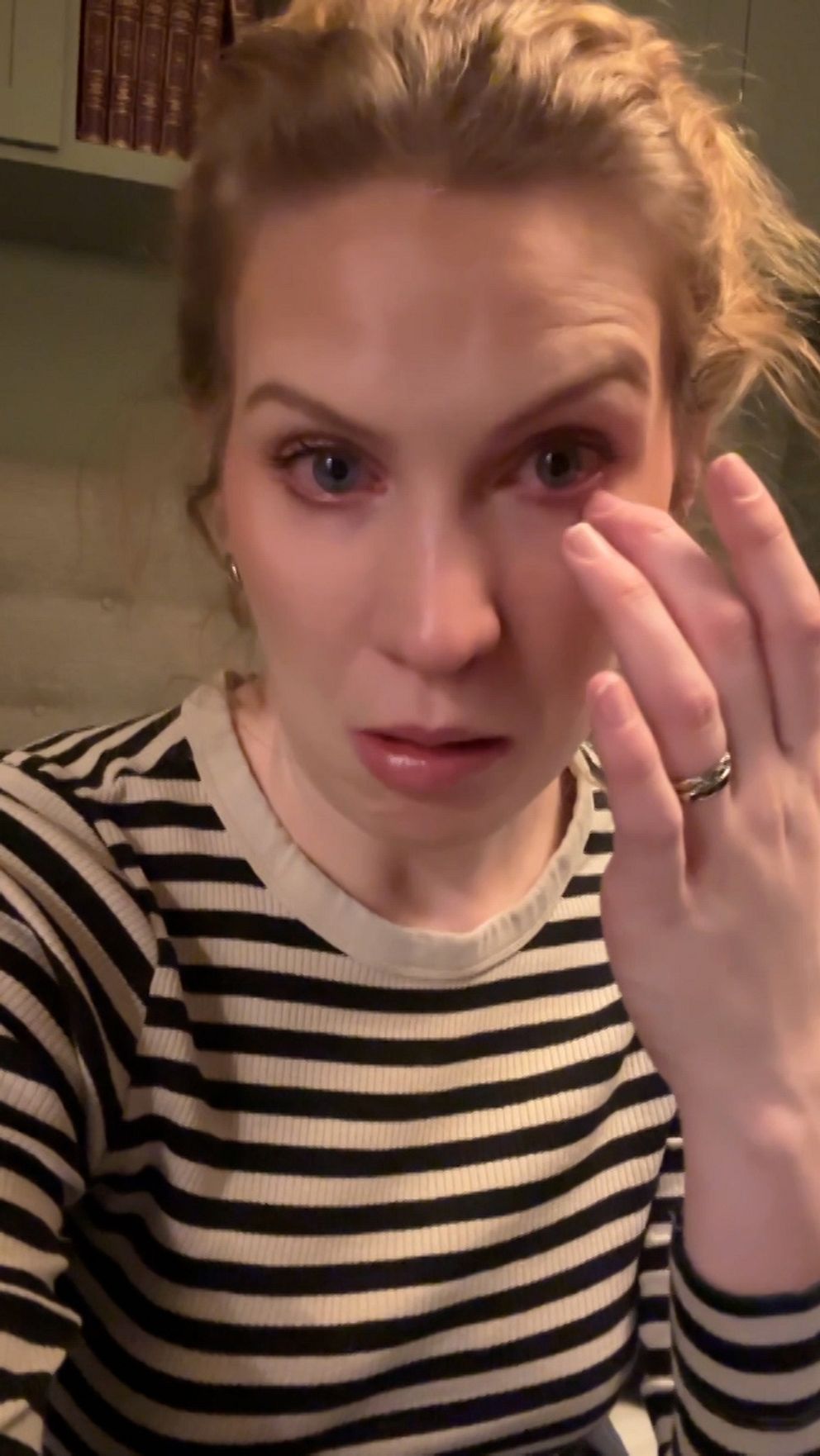Person i randig tröja sitter inomhus, böcker syns i bakgrunden.