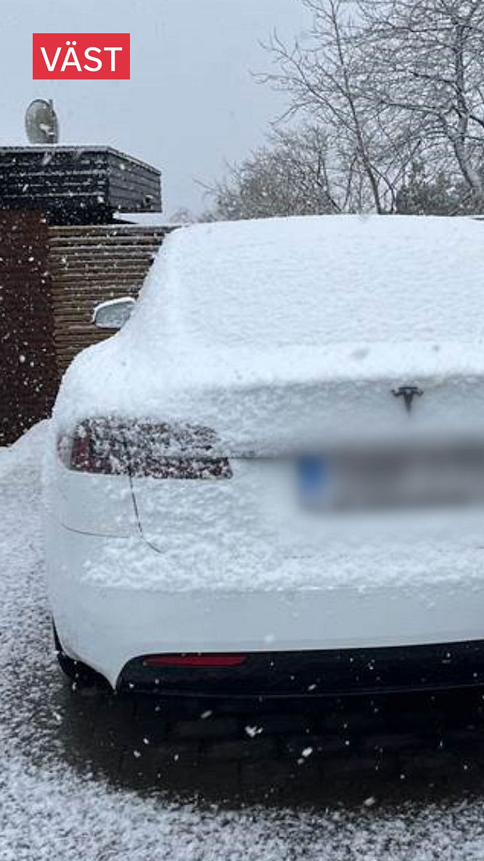 Vit Tesla täckt av snö, parkerad utomhus en vinterdag. Texten ”VÄST” synlig högst upp.