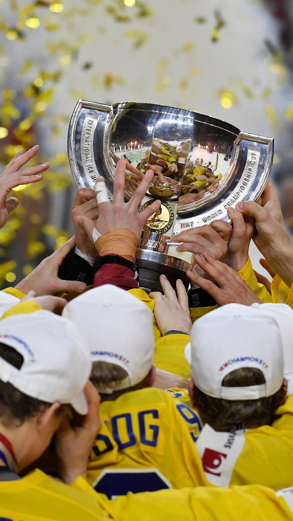 Svenska ishockeyspelare firar seger och lyfter en stor pokal, konfetti faller i bakgrunden.