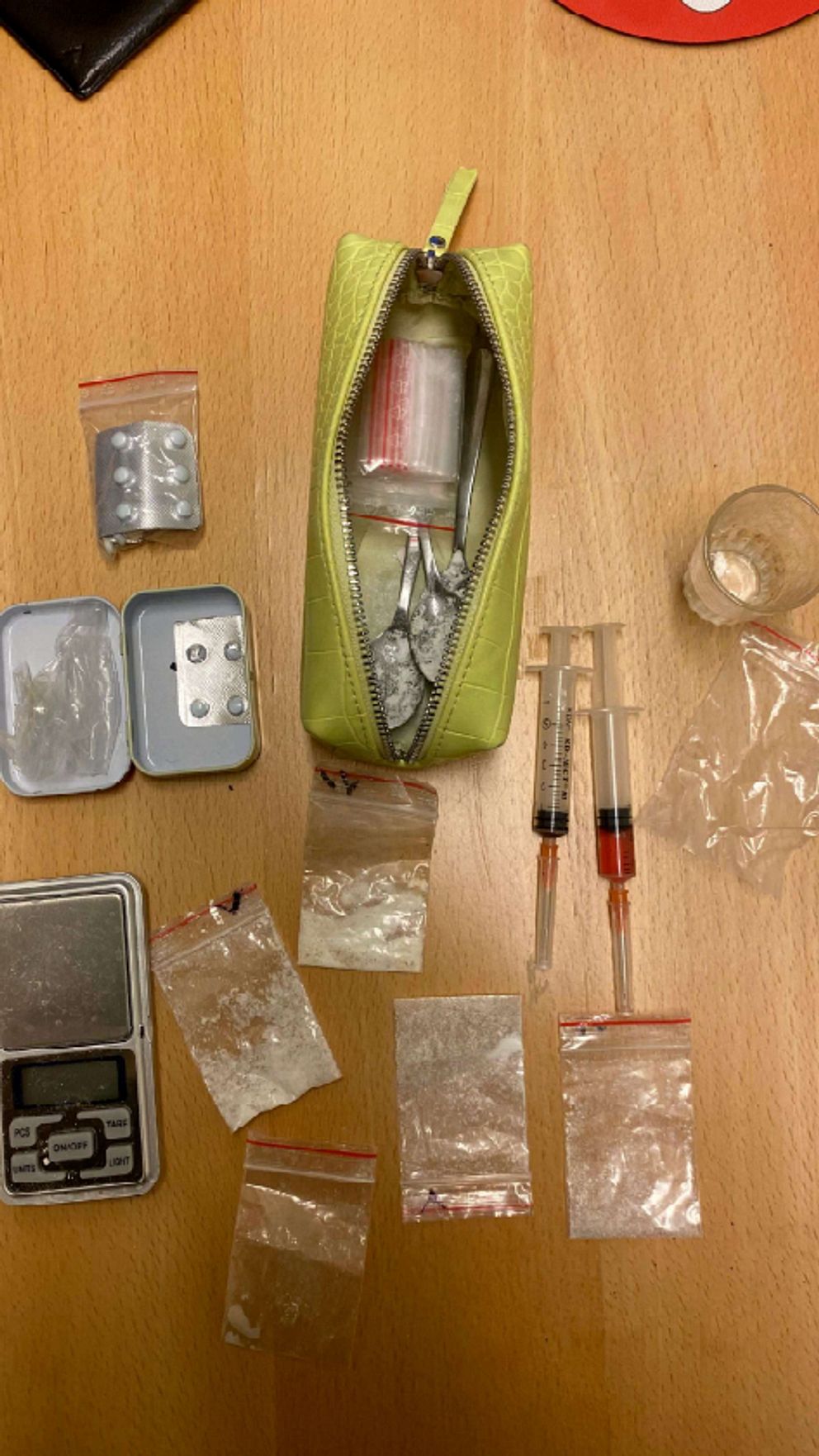 Narkotikarelaterade föremål på ett bord: våg, sprutor, plastpåsar med vitt pulver och en grön väska.