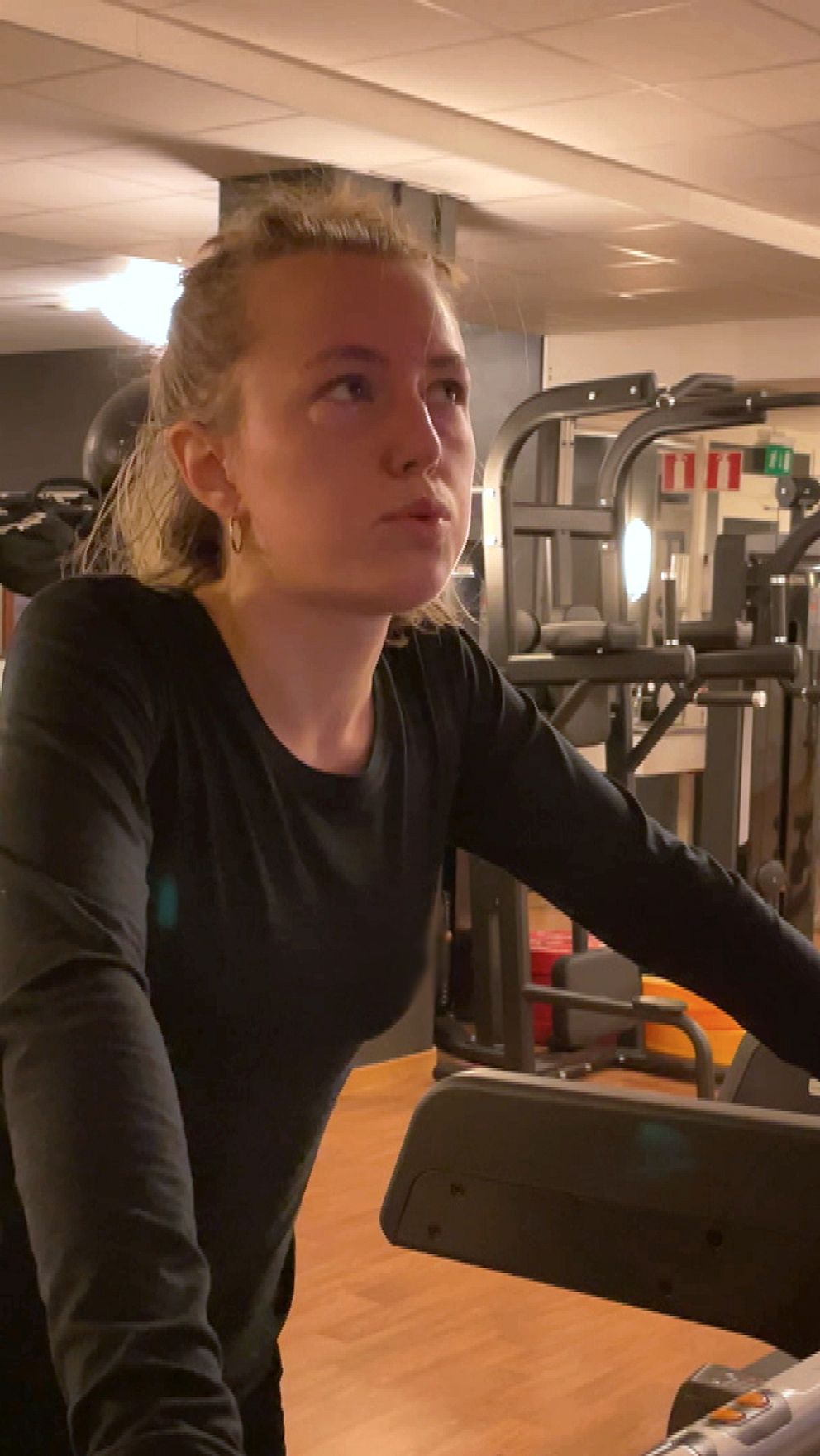 En person i träningskläder står vid en träningsmaskin i ett gym, med fokus på träning och fitnessutrustning i bakgrunden.