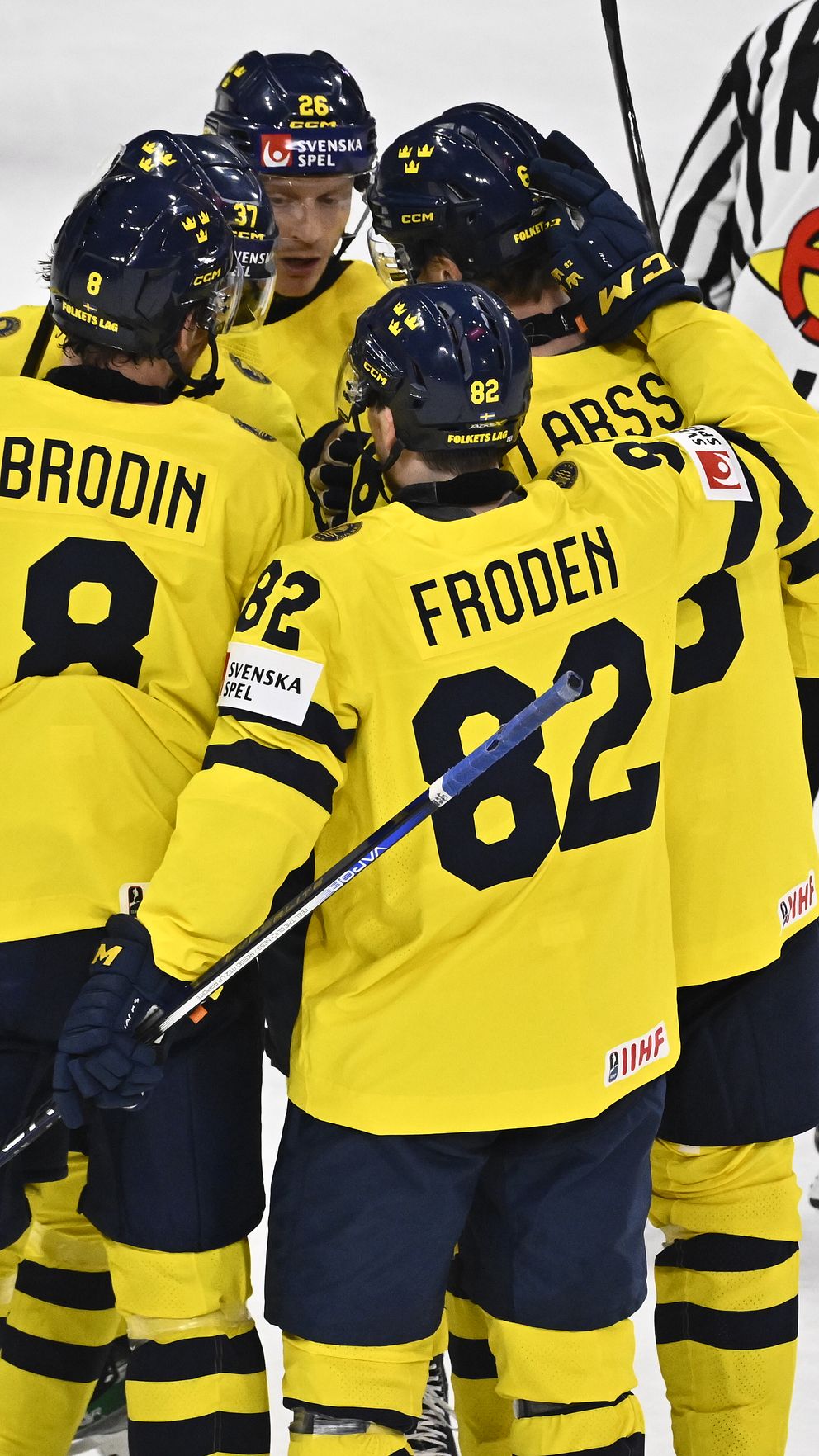 Svenska ishockeyspelare i gula tröjor kramas på isen efter ett mål. Domare i bakgrunden.
