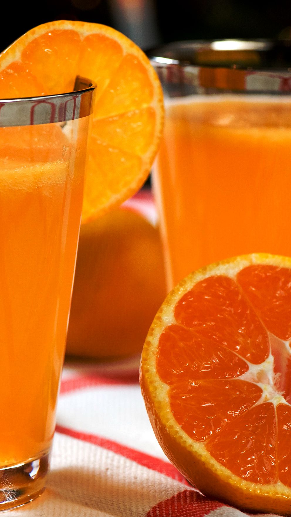 Två glas apelsinjuice med skivade apelsiner på en duk.
