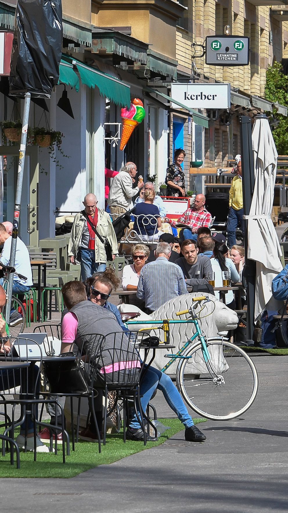 Människor njuter av soligt väder på uteservering vid en kafé och restauranggata.