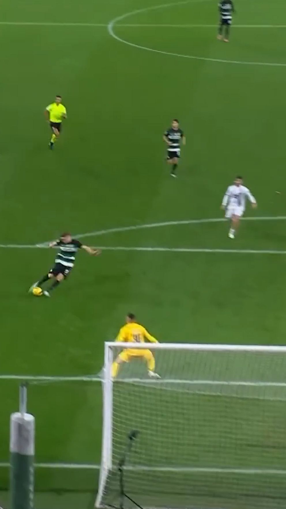 Fotbollsspelare skjuter mot mål, målvakt i gult förbereder sig för räddning.