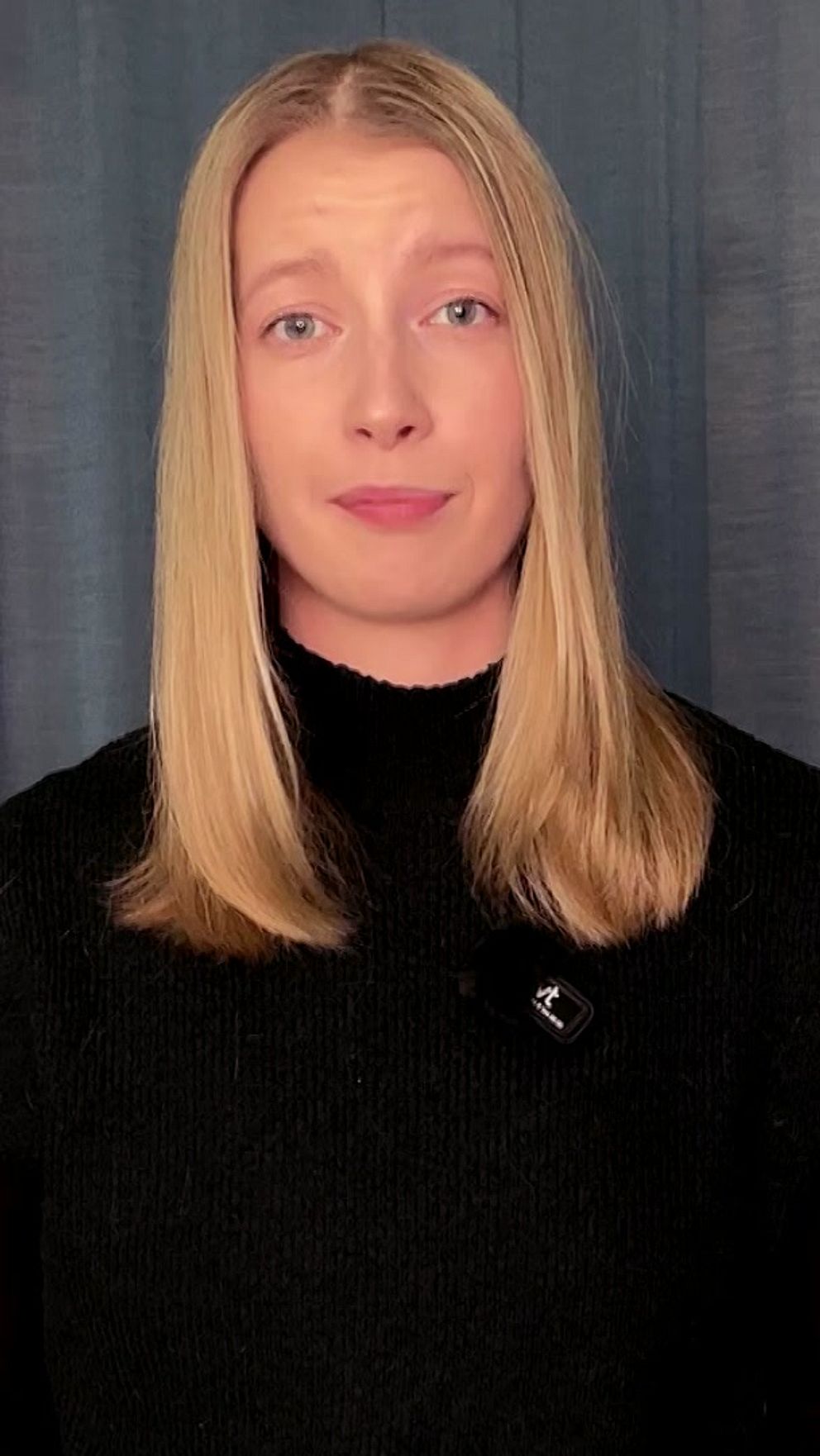 Person med långt blont hår framför en grå bakgrund.