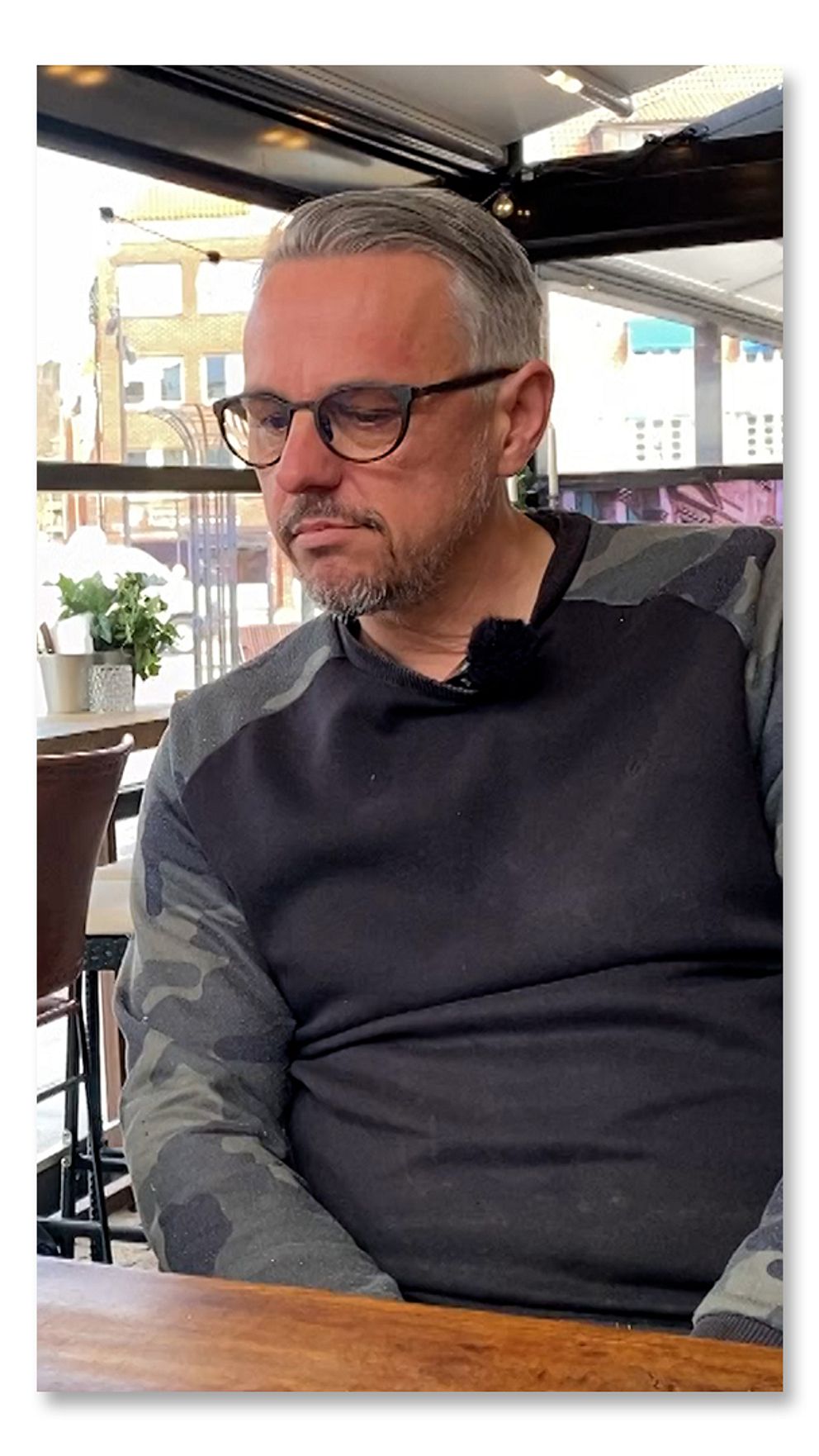 En person med glasögon sitter vid ett bord på ett café eller en restaurang.