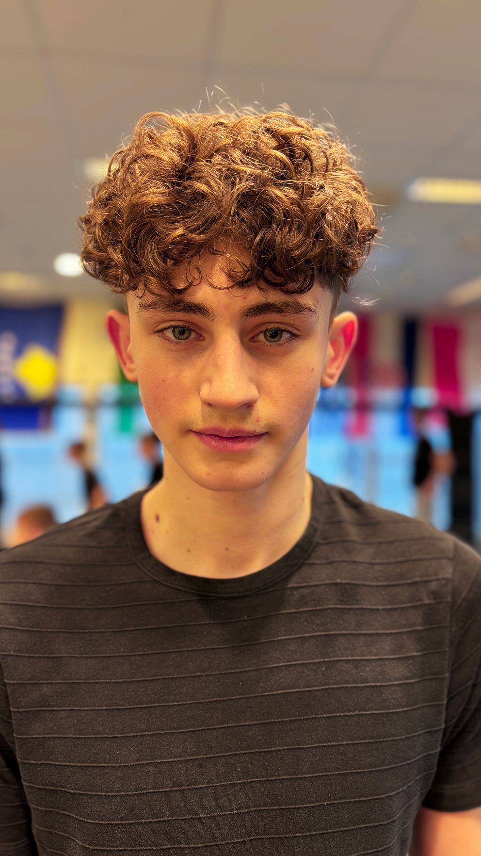 Ung man med lockigt hår i Västerås fight clubs lokal på Bäckby i Västerås med flaggor i bakgrunden.